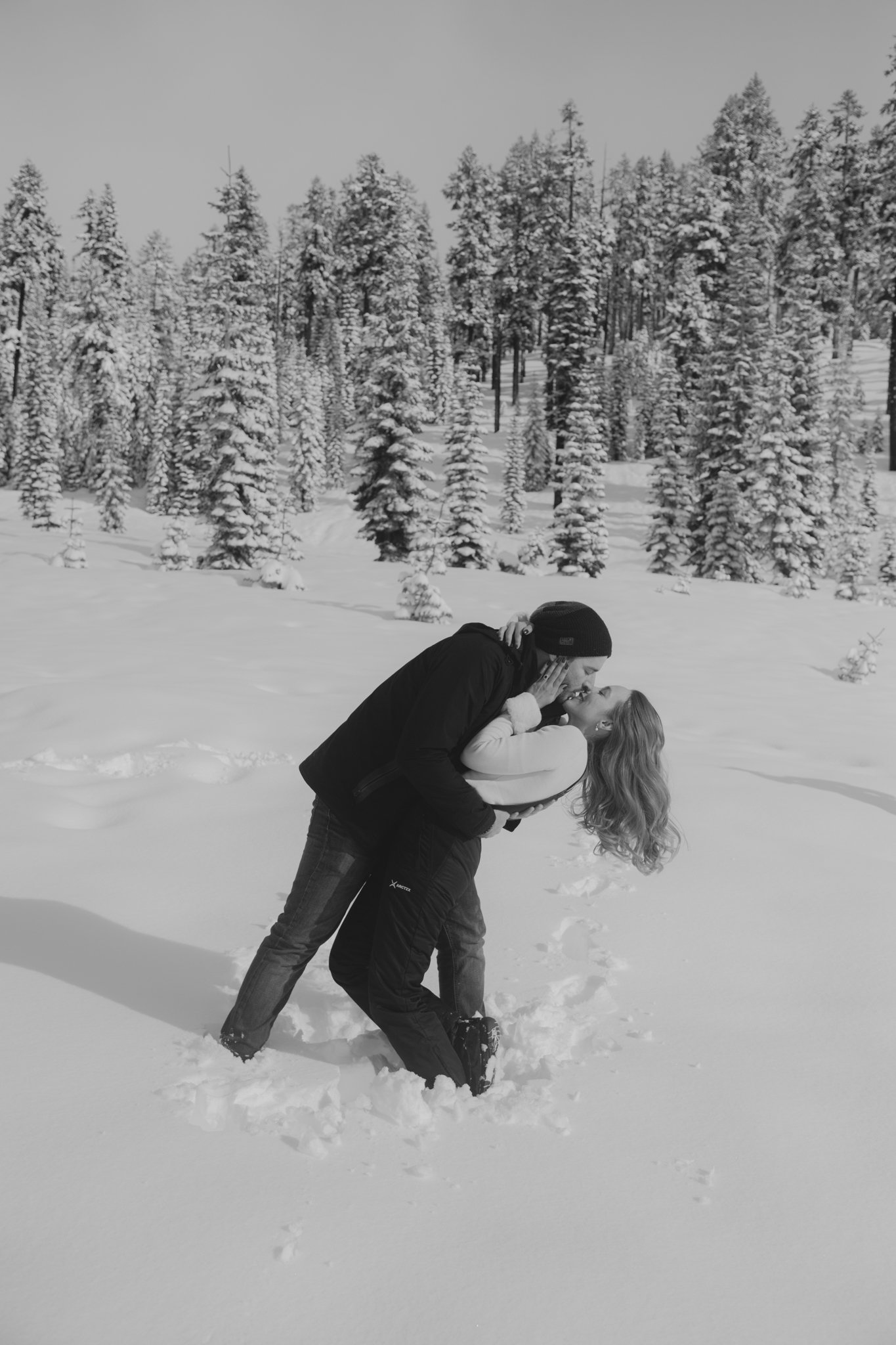 Una pareja en un paisaje nevado, compartiendo un momento romántico y abrazándose en la nieve, rodeados de árboles cubiertos de hielo.