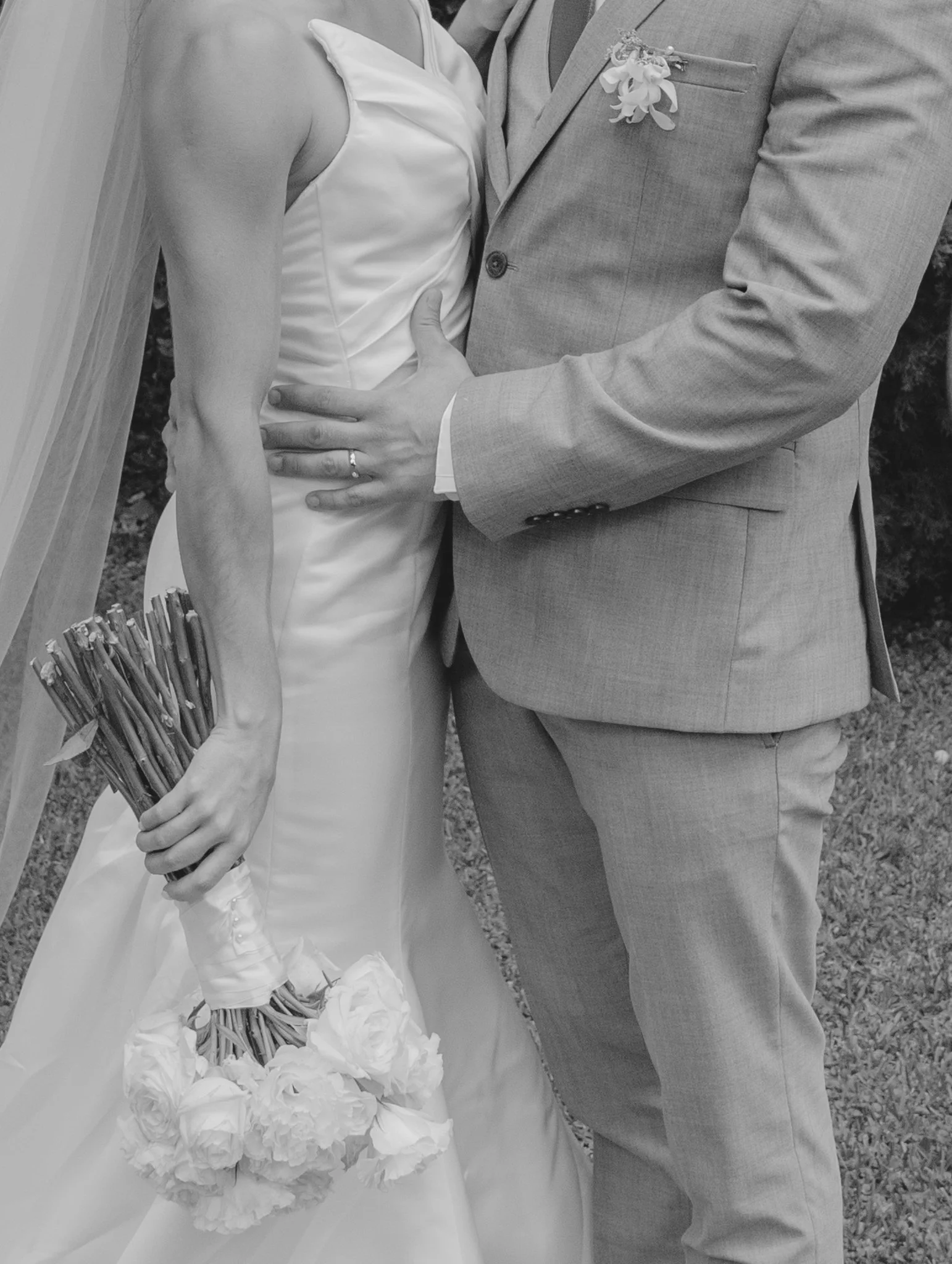 Pareja en boda, ella con vestido de novia y ramo de flores, él con traje, en un abrazo en exteriores.