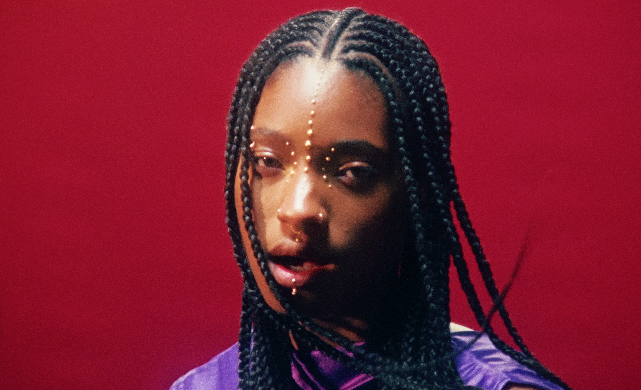 A woman with braided hair and facial jewelry against a red background.