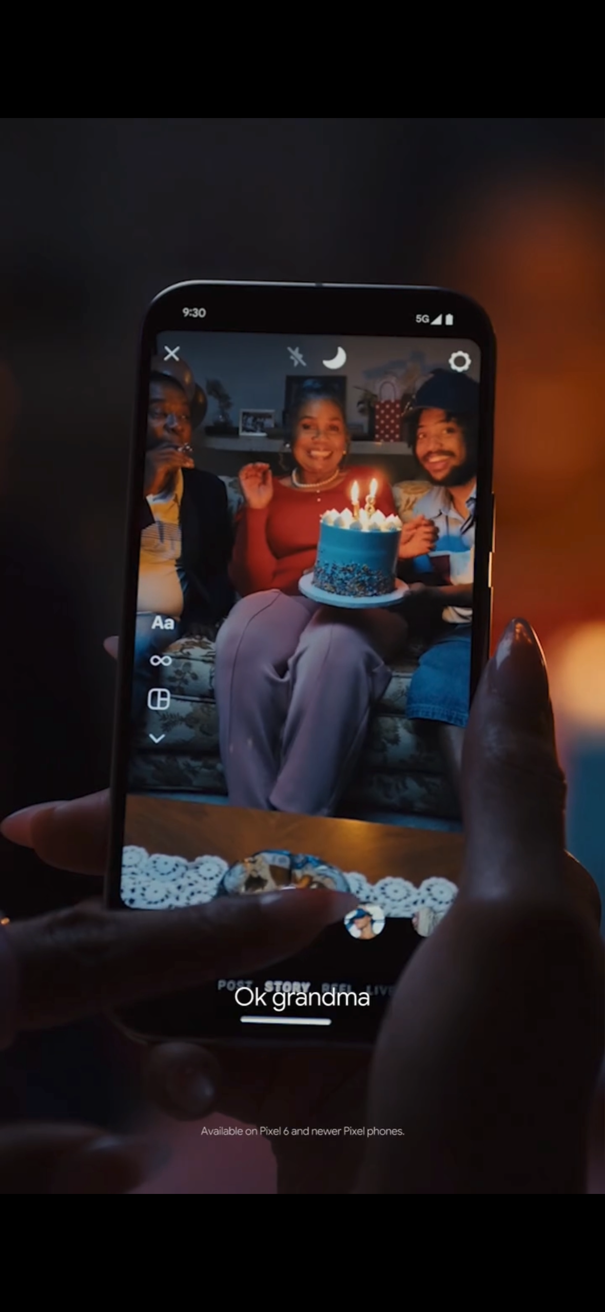 Person taking a photo of a birthday celebration on a smartphone, showing a woman smiling with a birthday cake with lit candles, flanked by two men, in a cozy indoor setting.