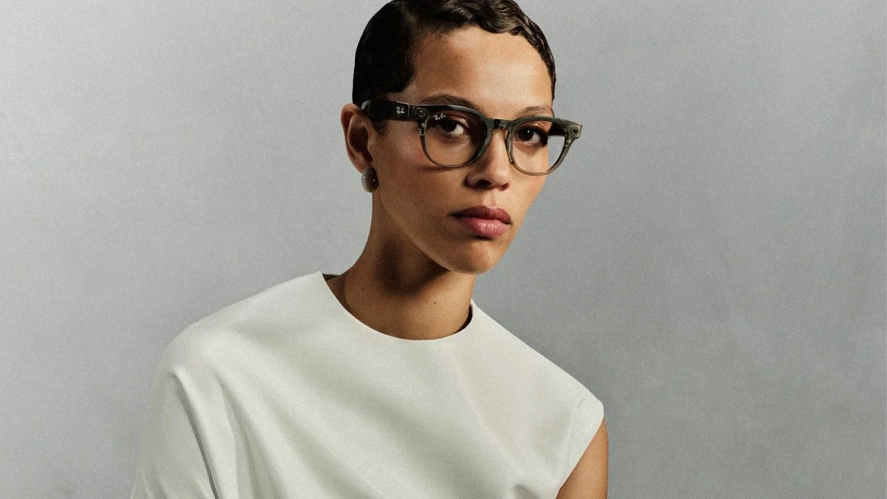 Portrait of a woman with short dark hair, wearing glasses and a white top, against a gray background.
