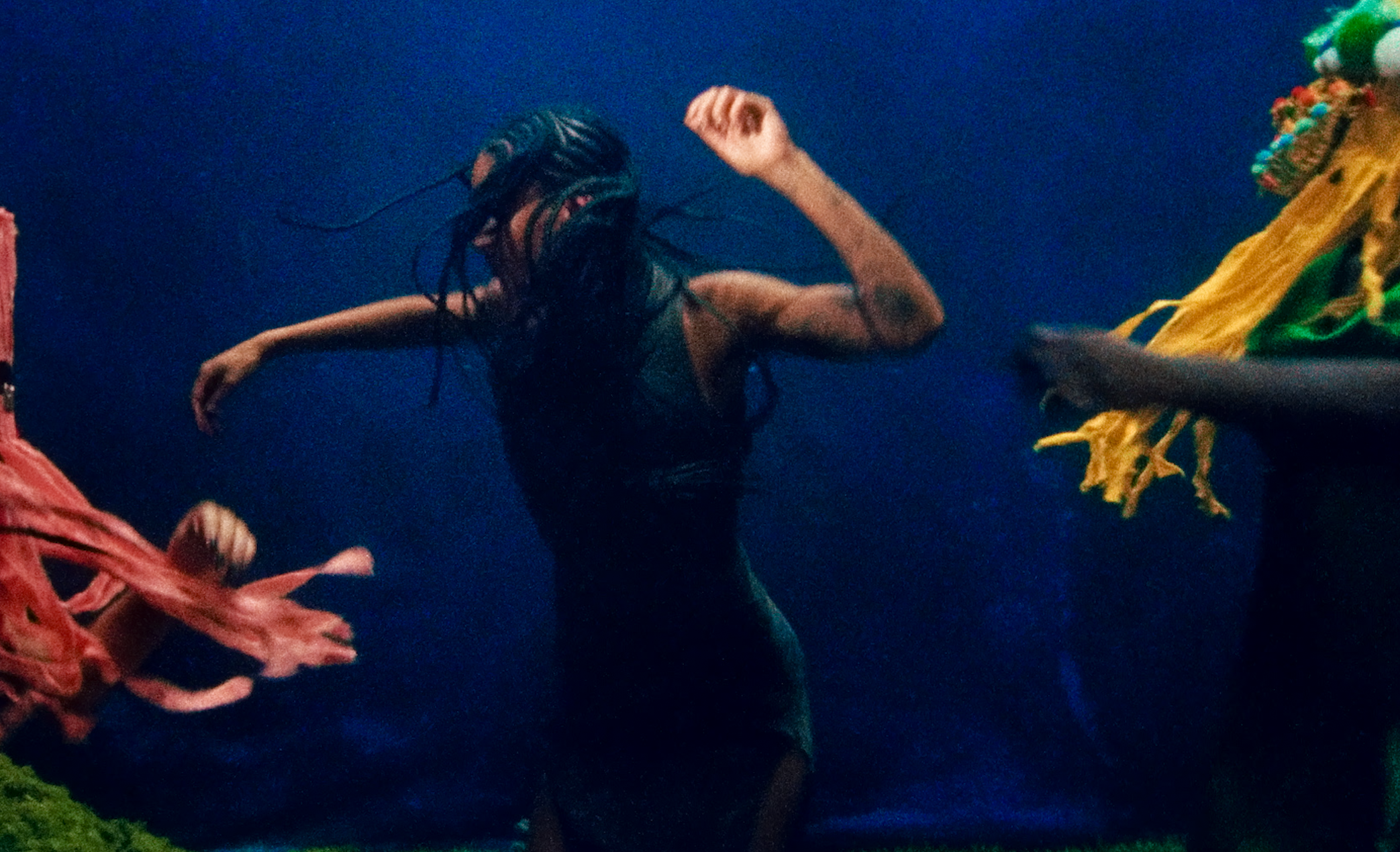 Person with long braided hair dancing or performing on a stage with colorful decorations and fabric hanging around.