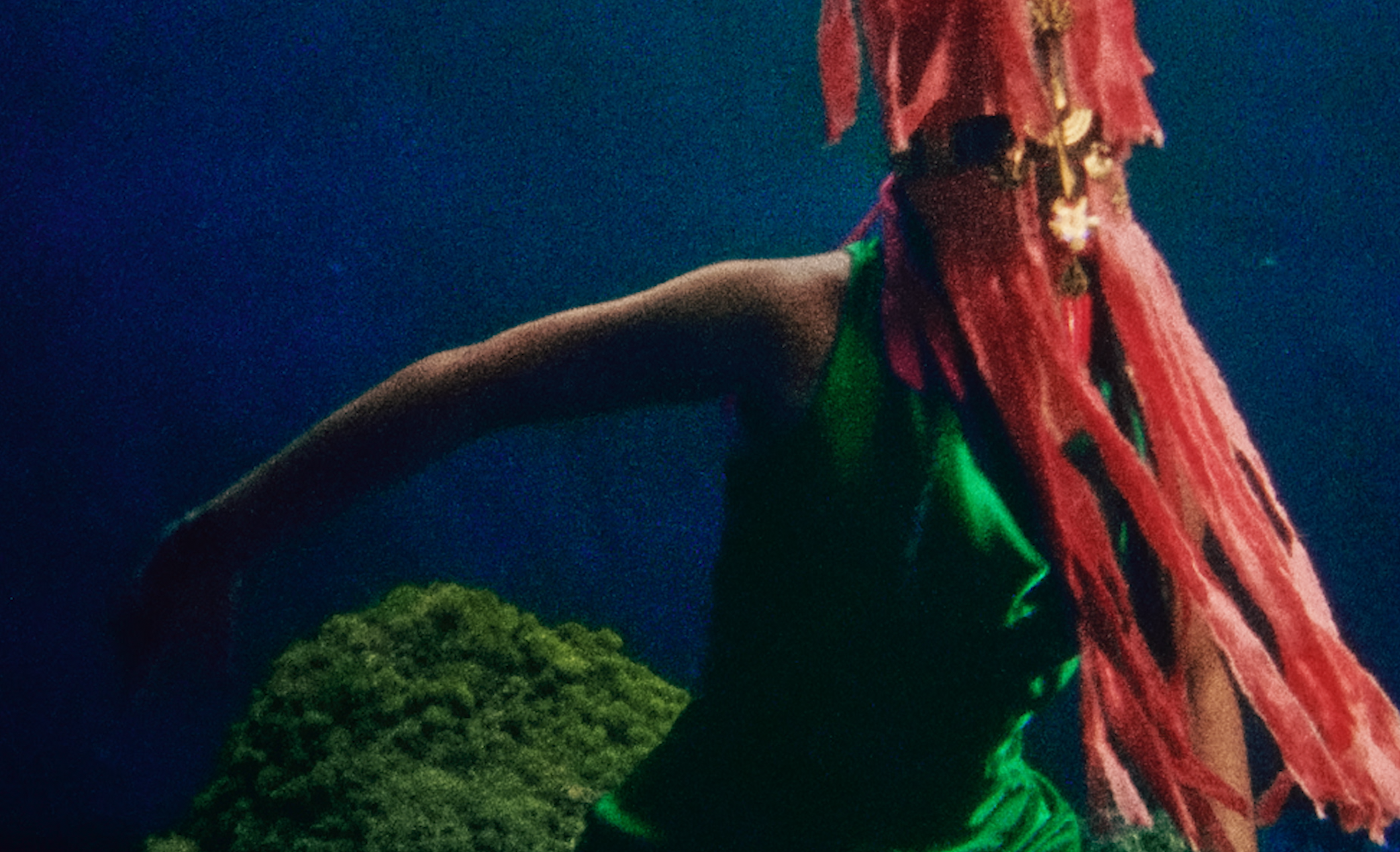 A large statue with red dreadlocks, wearing a bright green outfit, set against a dark night sky and green foliage.
