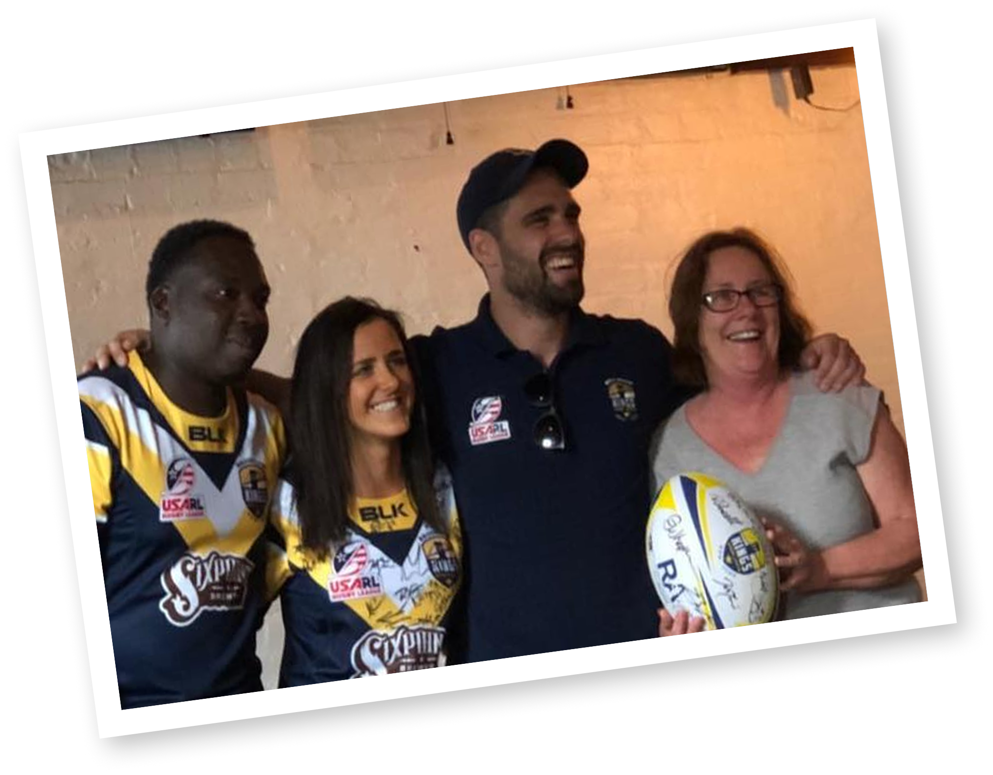 Group of people smiling and posing for a photo at an indoor event, some wearing sports jerseys and medals.