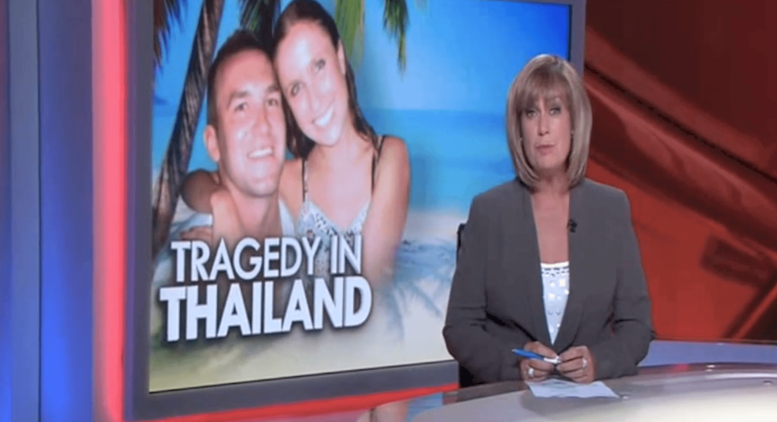 A female news anchor in a gray blazer sitting at a news desk, with a large screen behind her displaying a tropical scene and the text 'Tragedy in Thailand' along with an image of two smiling women in swimwear.