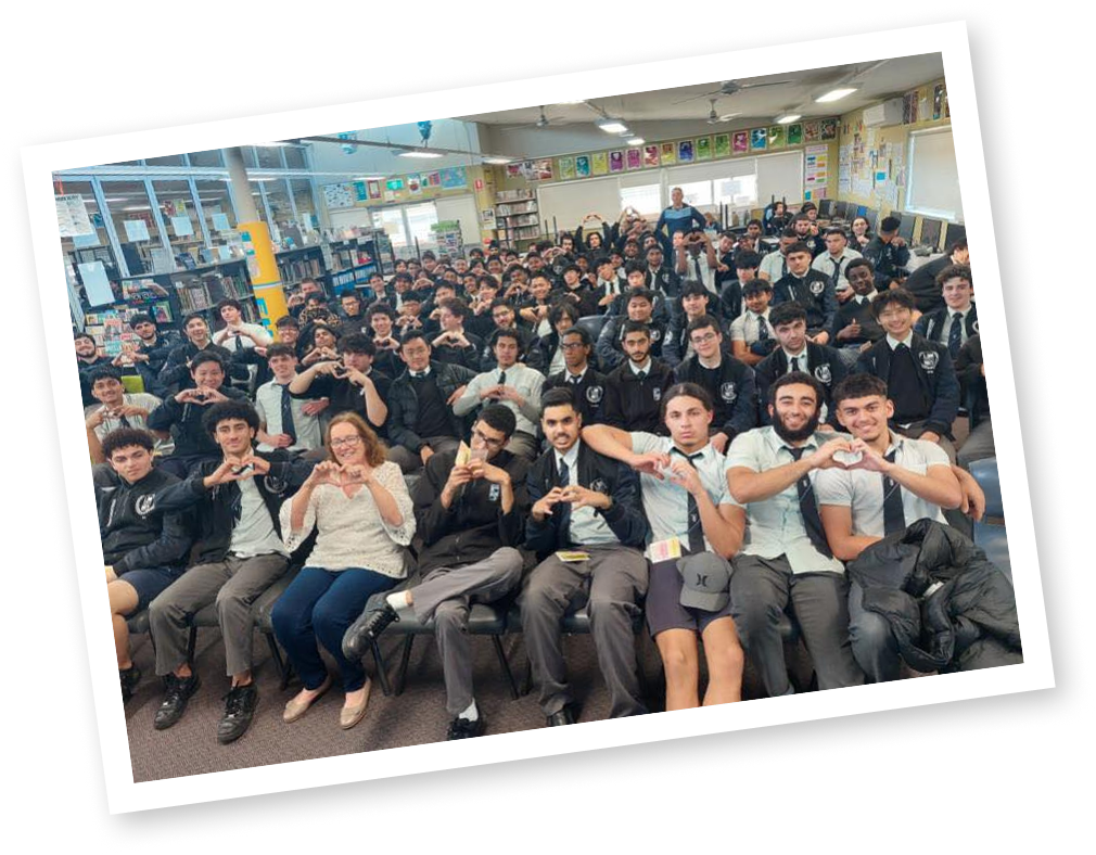 Group of students in a classroom, some making heart signs with their hands, posing for a group photo.