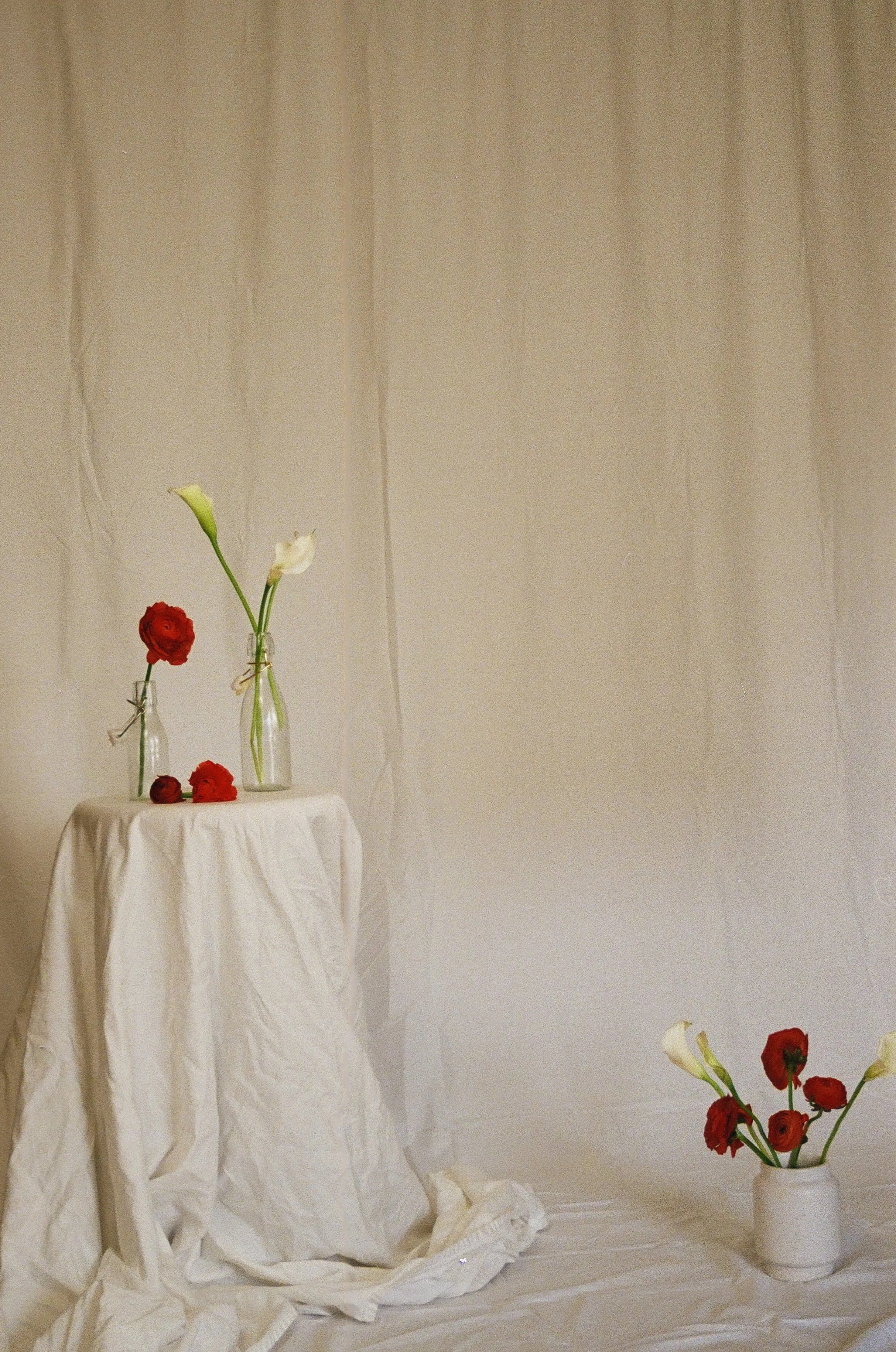 Flowers in vases on a draped white cloth against a neutral background.