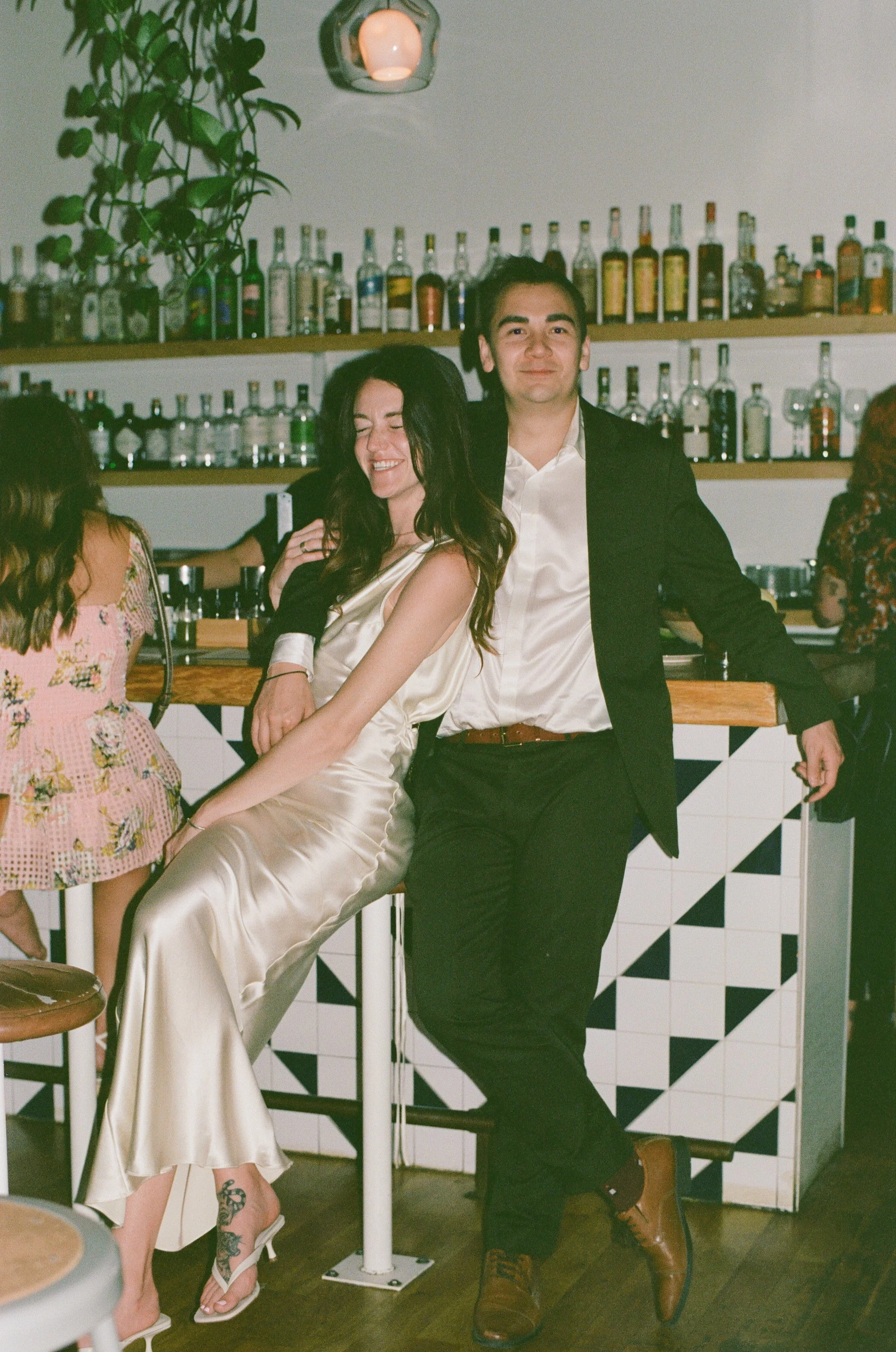 A bride and groom smiling as they take in their wedding guests. they had their reception at their neighborhood dive bar. 