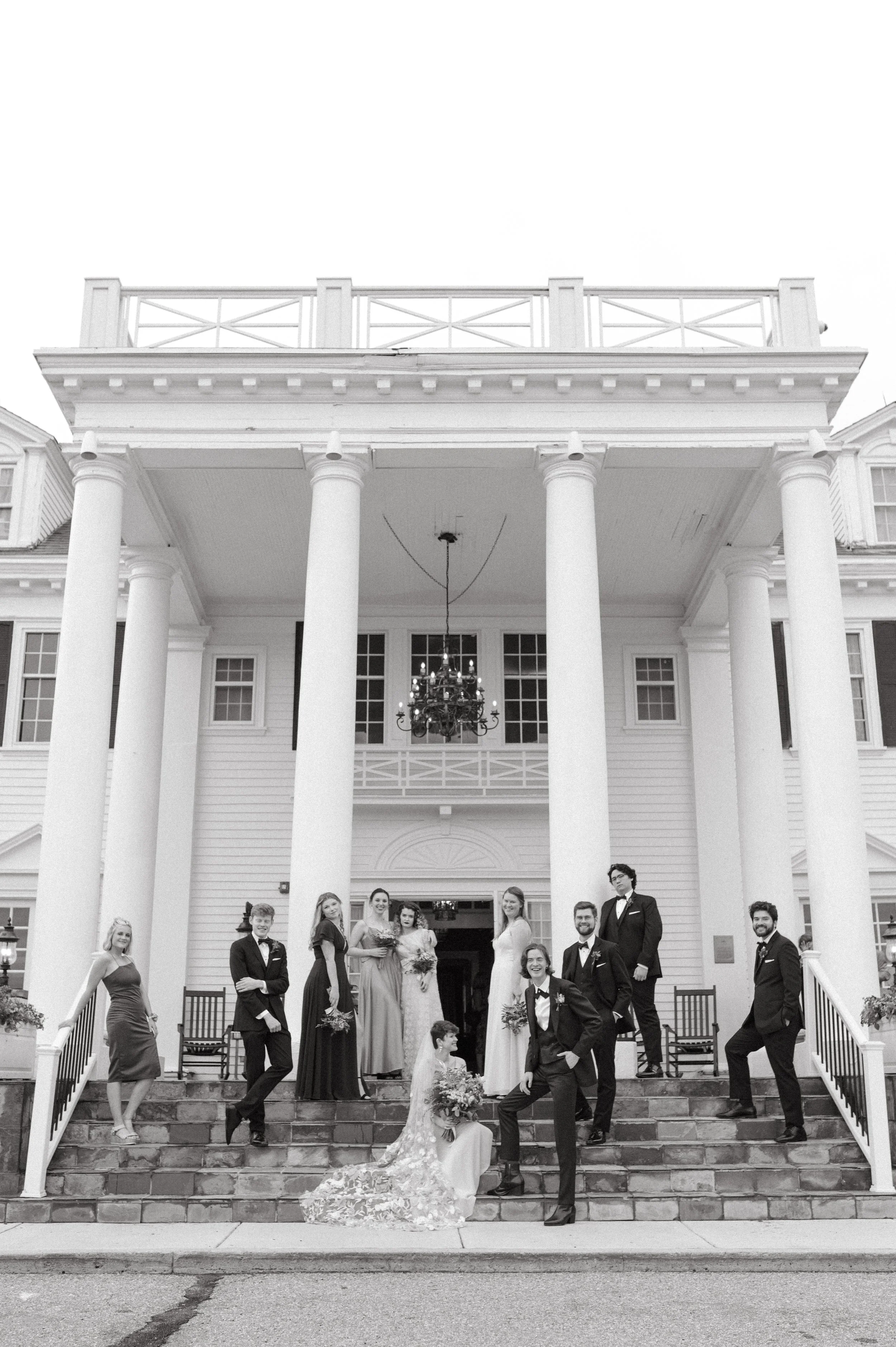 A wedding party posed on the steps of a large, elegant mansion with classical columns, including brides, grooms, bridesmaids, and groomsmen. this was outside of the manor house in Denver Colorado. 