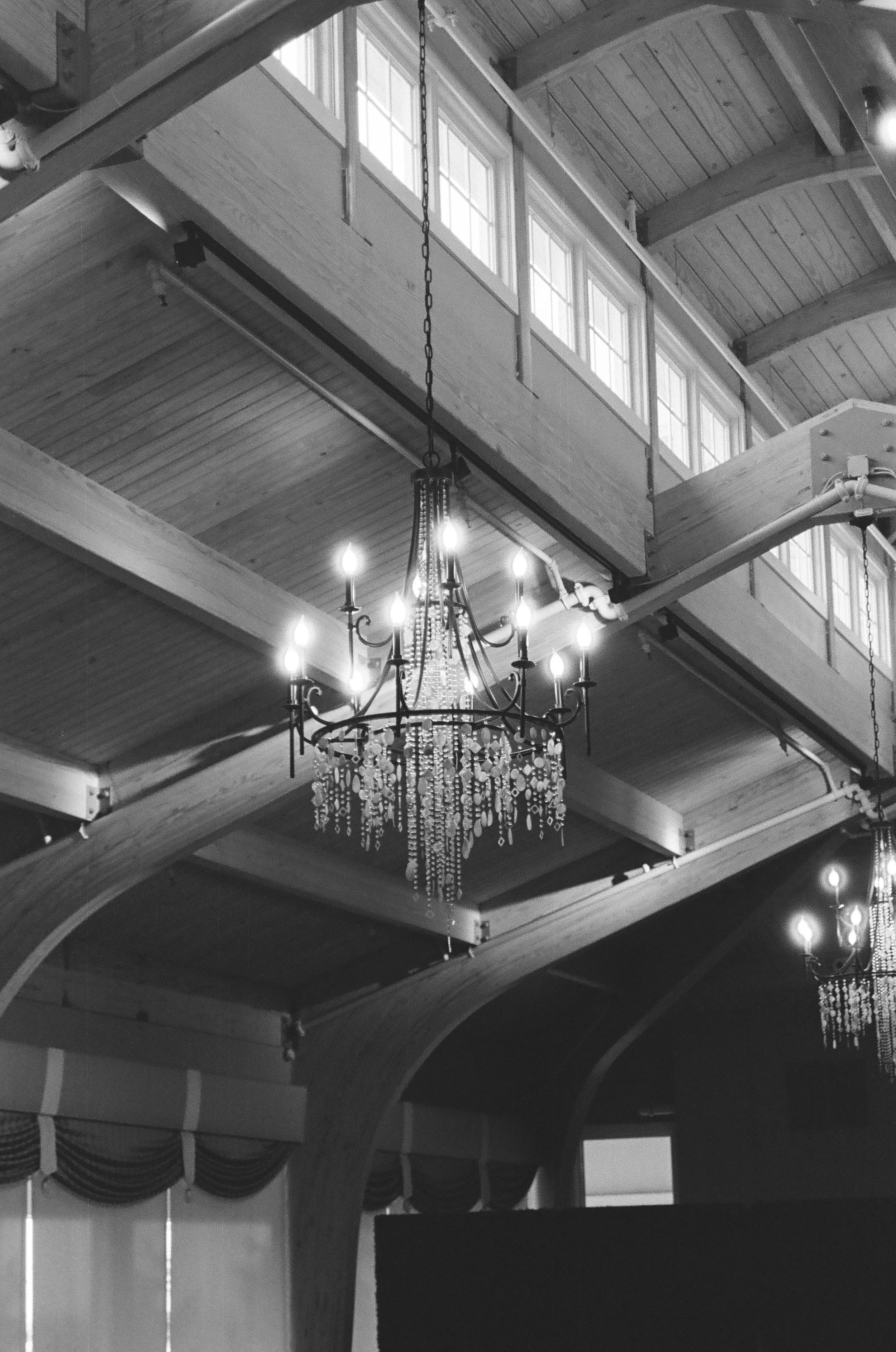 Interior of a wooden building with a chandelier hanging from the ceiling, multiple windows with natural light, and decorative curtains.