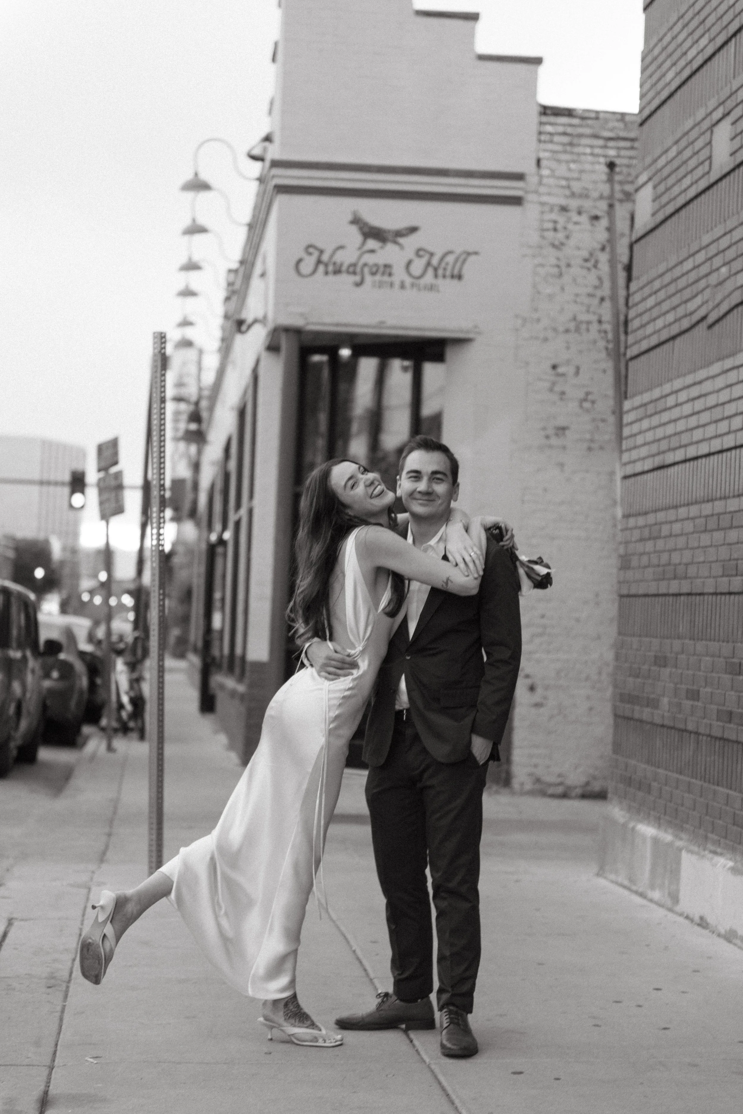 A bride and groom embracing on the city sidewalk in front of Hudson Hill in Denver Colorado.