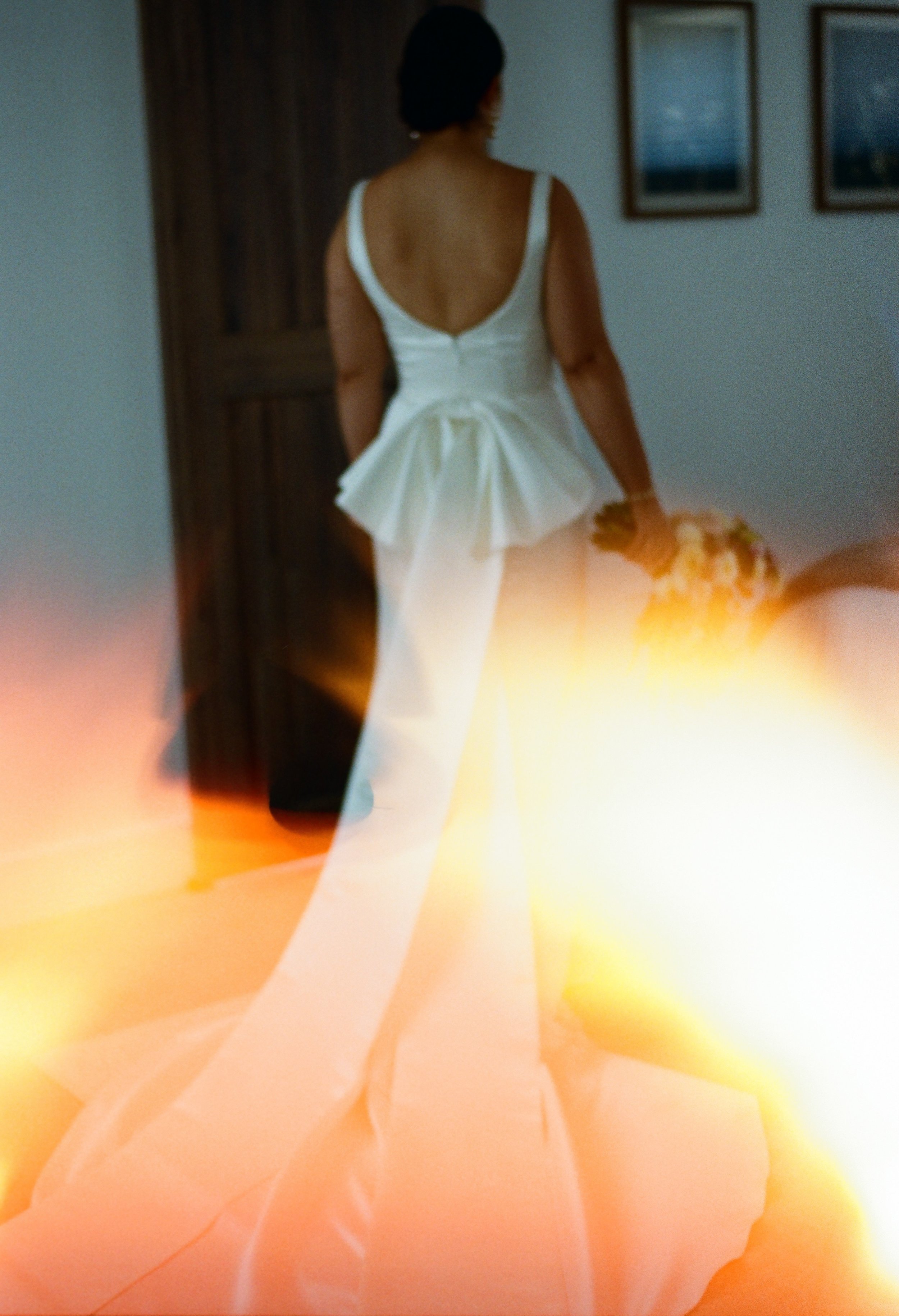 A film photo of a bride dressed in a white gown holding a bouquet with a fun light leak. 