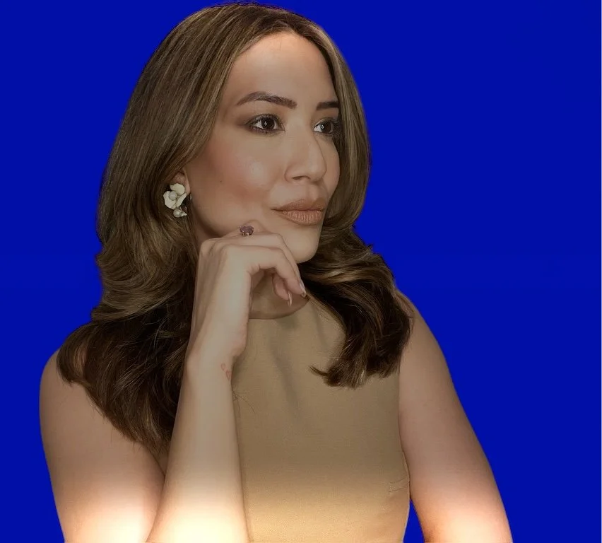 Portrait of a woman with light brown hair and light skin, wearing a sleeveless beige top, earrings, and a ring, against a solid blue background.