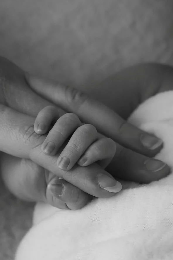 Close-up of a small child's hand grasping an adult's finger.