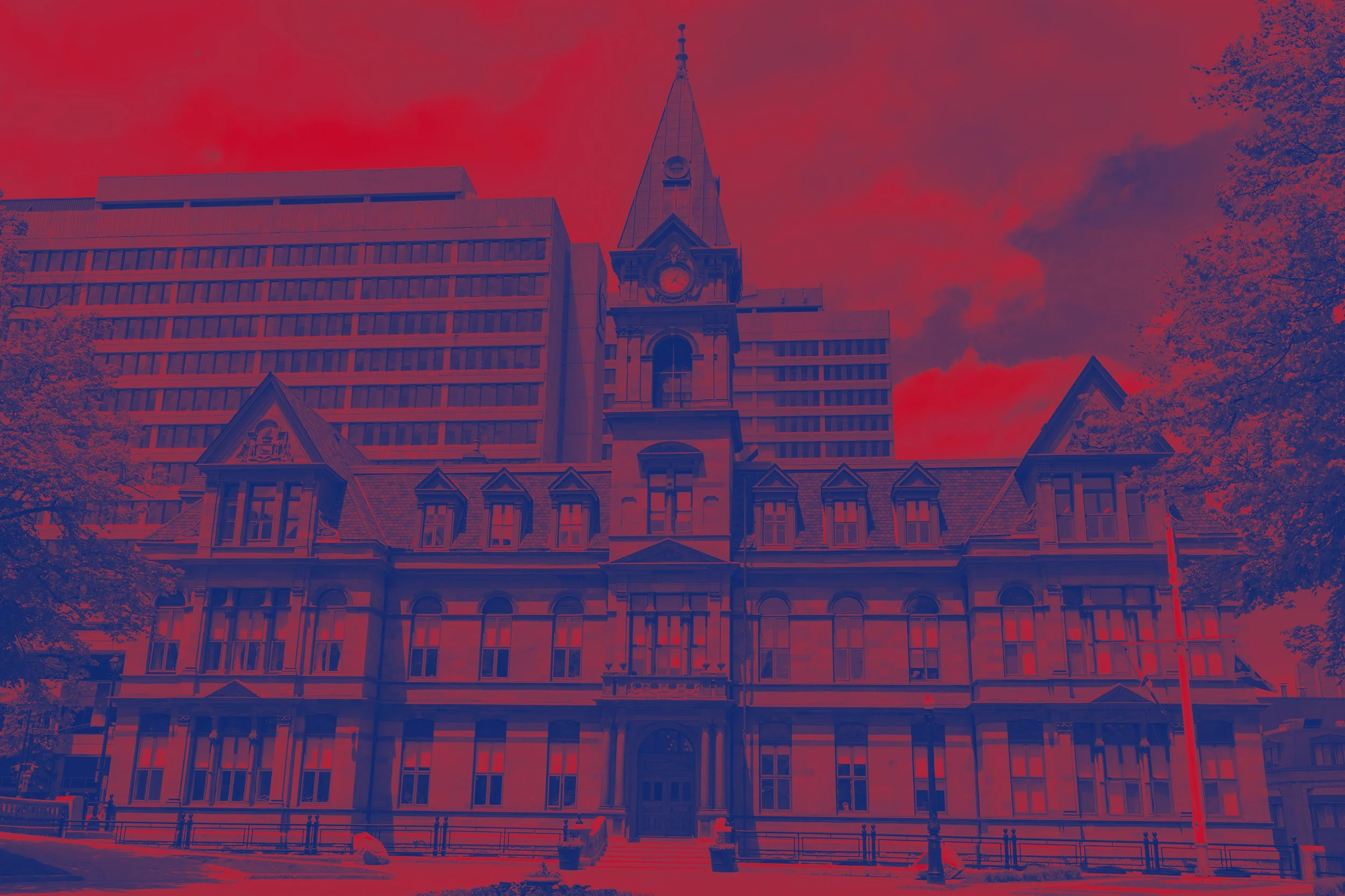 Historic courthouse building with a clock tower against a cloudy sky, with modern office building in background