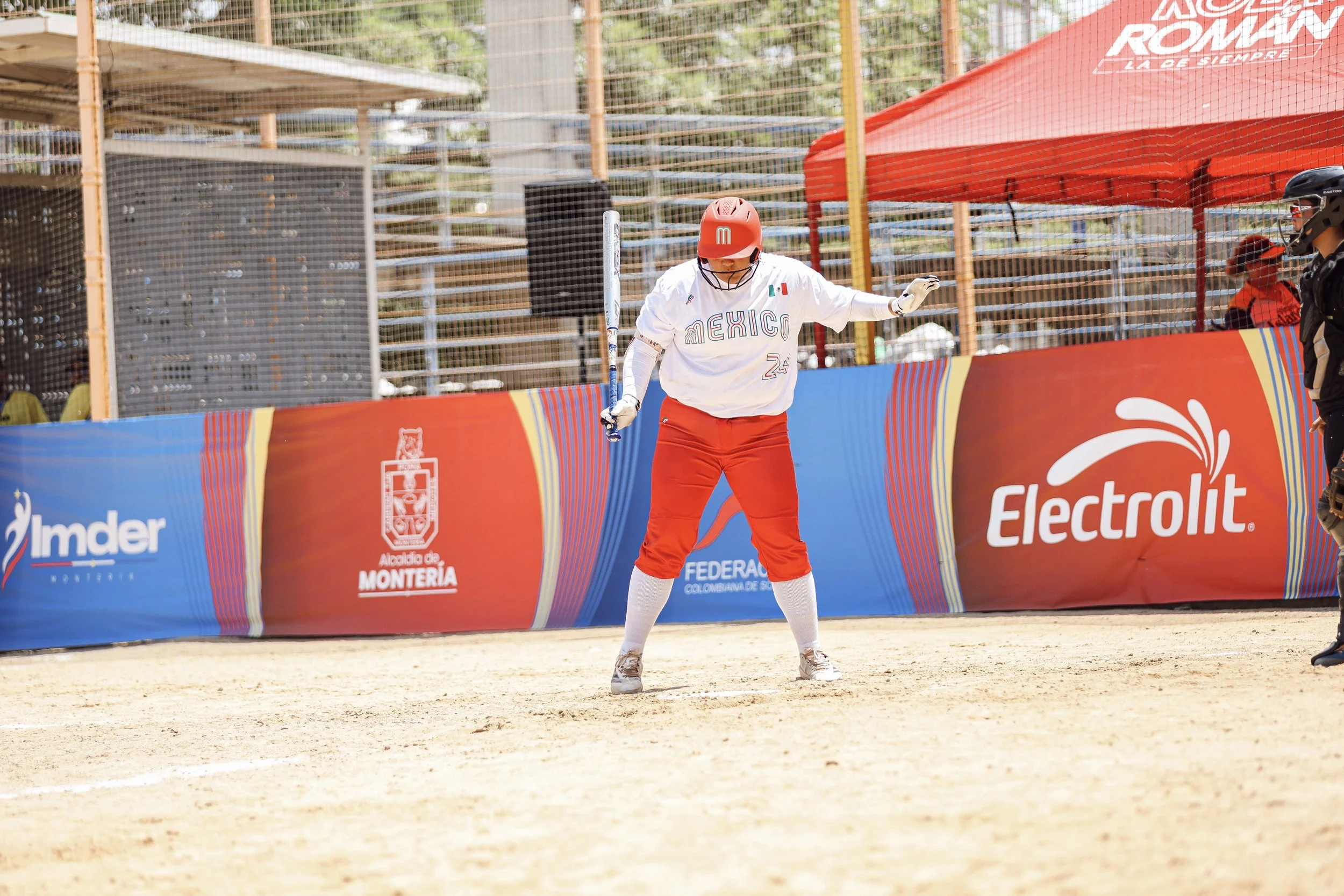 Mya Perez, Aggie Softball player,  in a Team Mexico jersey at home plate, ready to swing softball bat.