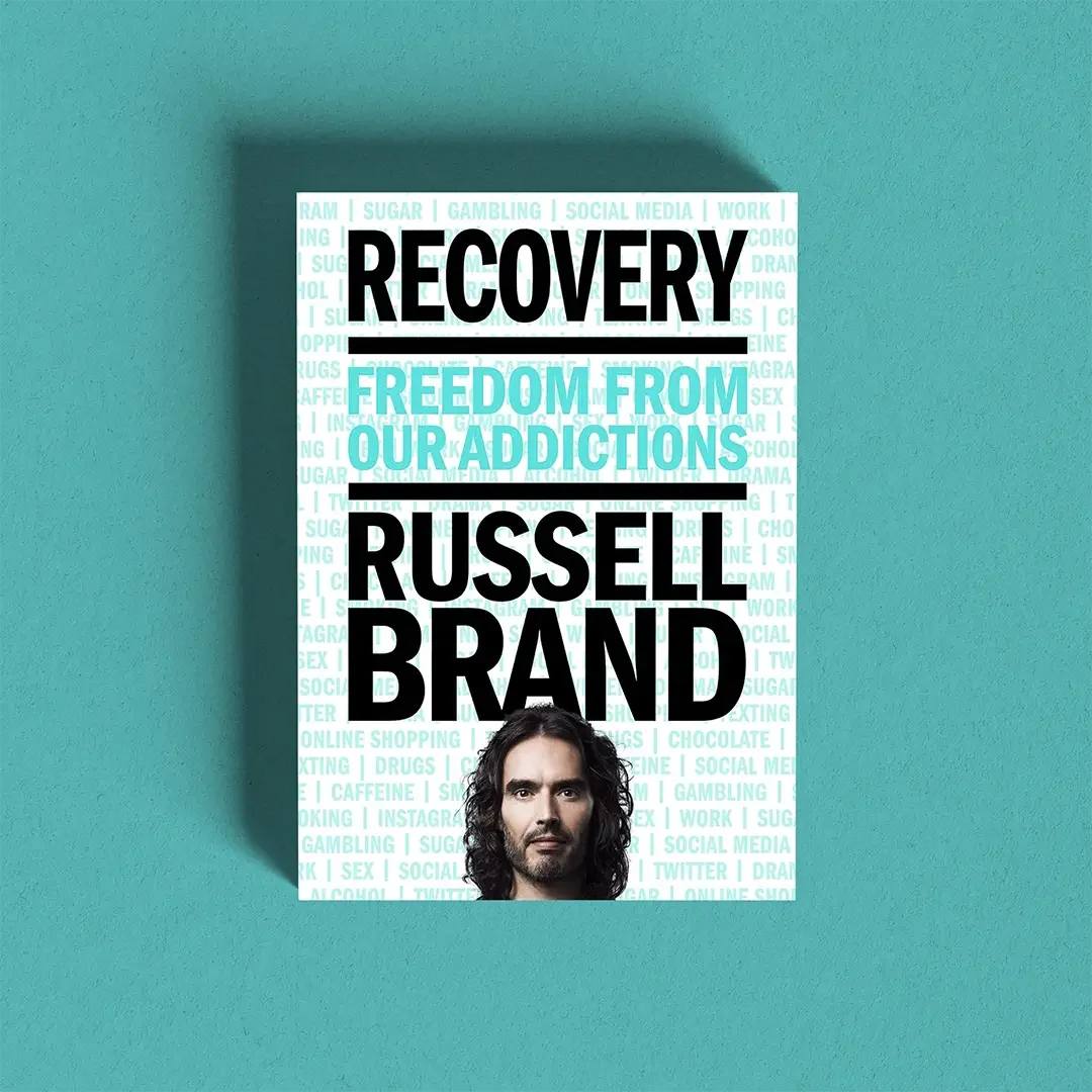 Book cover titled "Recovery: Freedom from Our Addictions" by Russel Brand, featuring a portrait of the author at the bottom against a light background with various words related to addiction and recovery.