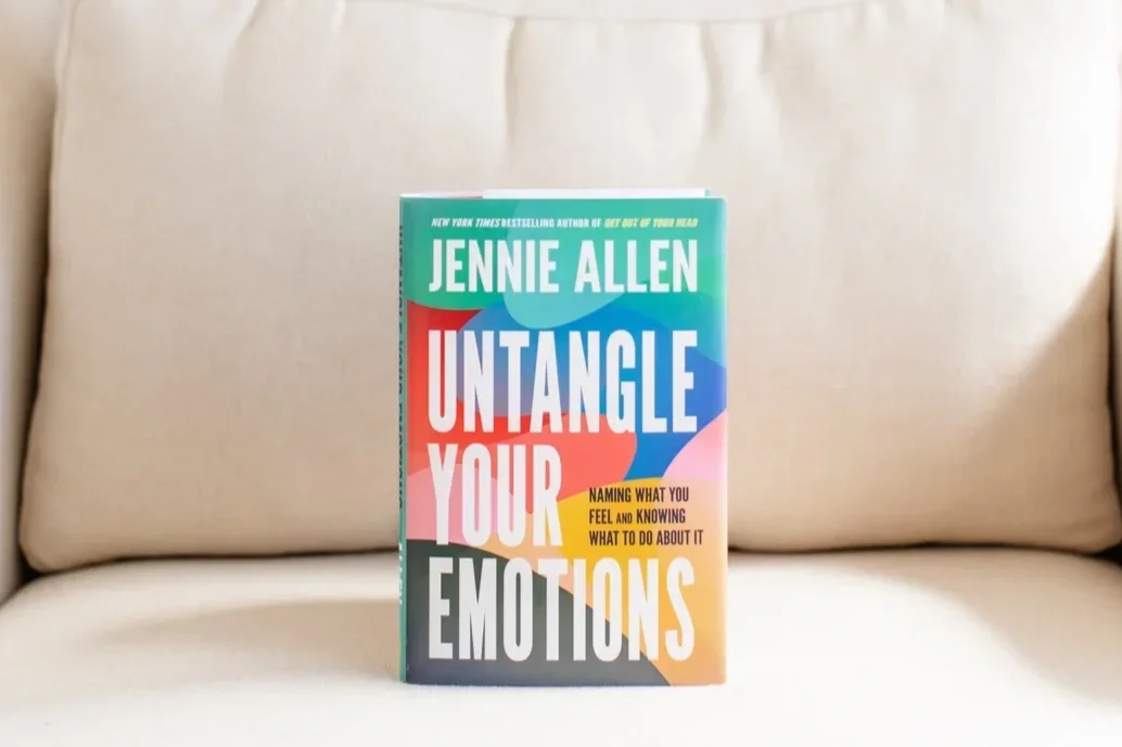 A book titled "Untangle Your Emotions" by Jennie Allen standing upright on a beige couch.