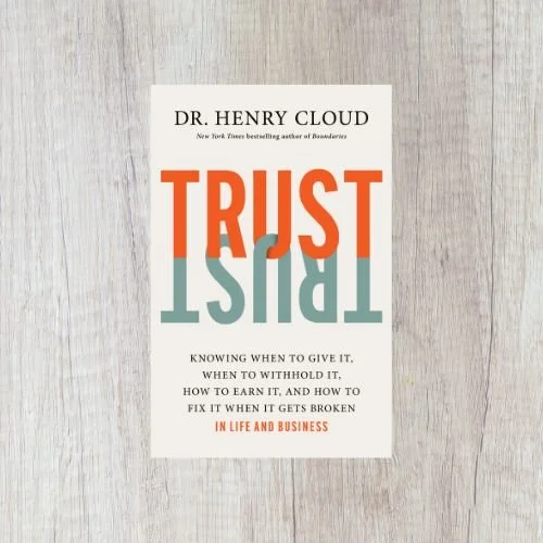 A book titled "TRUST" by Dr. Henry Cloud, placed on a light wood surface.