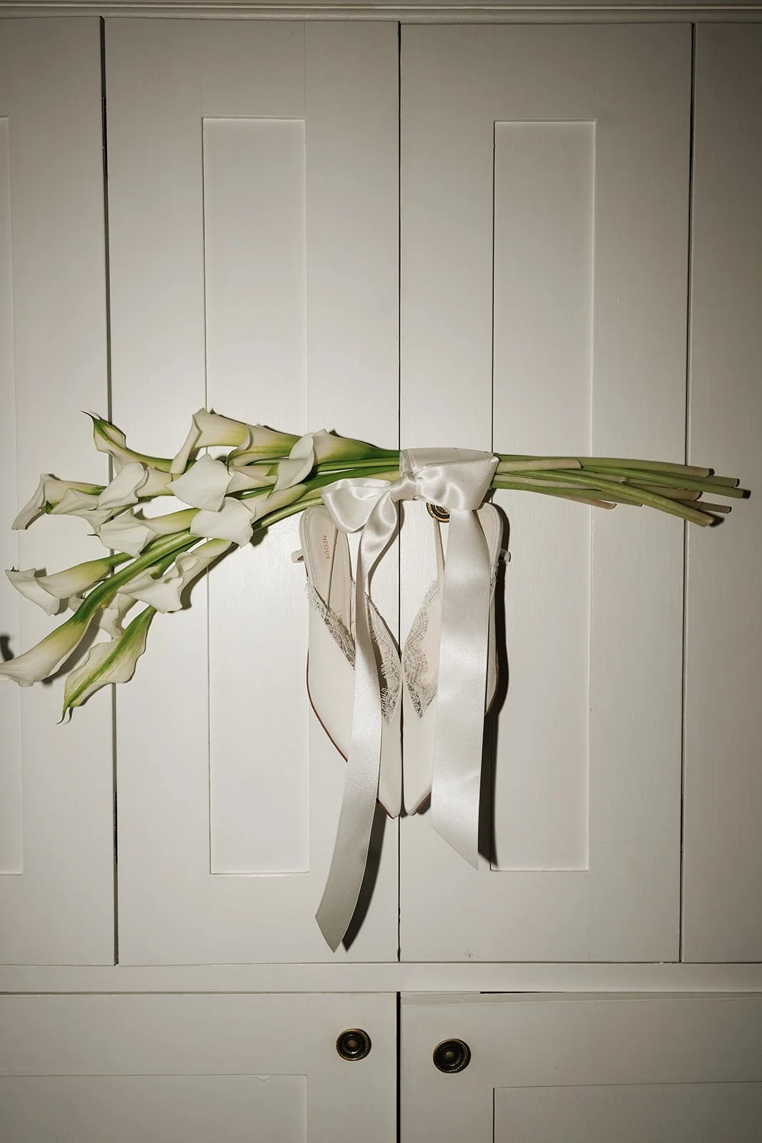 A bunch of white calla lilies tied with a white satin ribbon, resting on a white wooden cabinet.