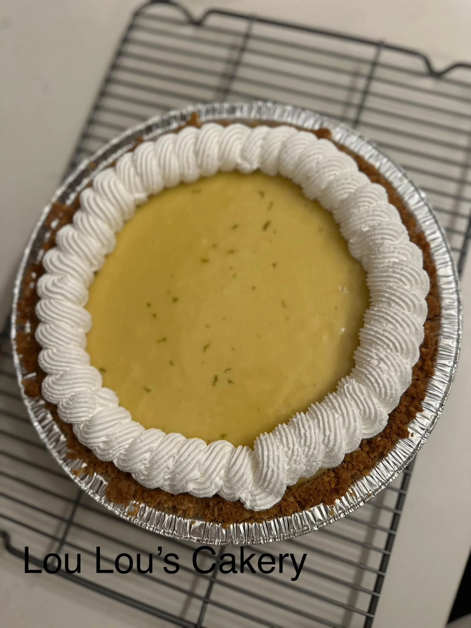 A lemon tart with a decorated crust and piped whipped cream border on a wire rack.