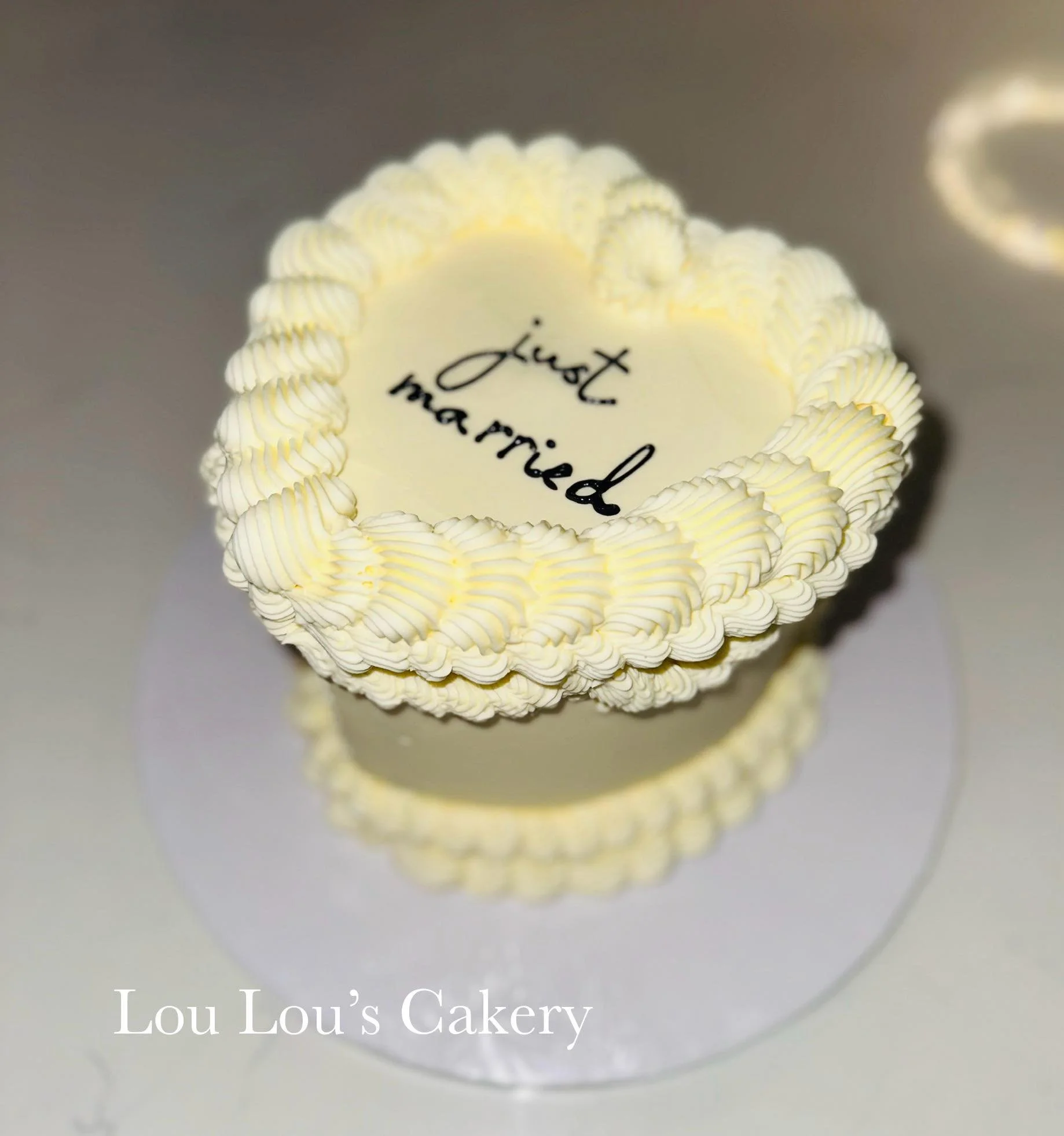 A round white cake with decorative piping around the edges, displaying the words 'just married' written in black icing on top.