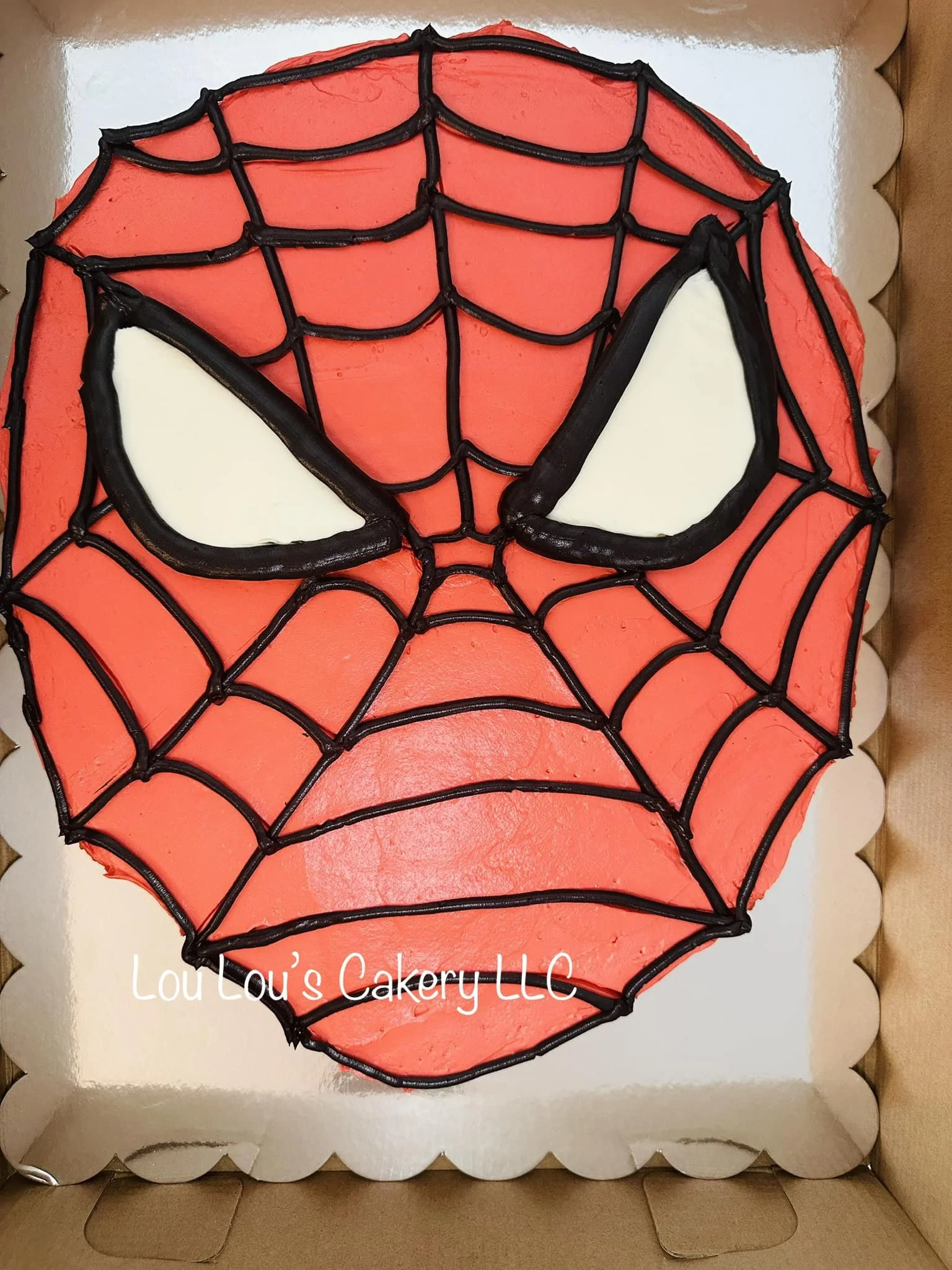 Cake decorated with Spider-Man's mask, featuring red icing, black icing web pattern, and white icing eyes.
