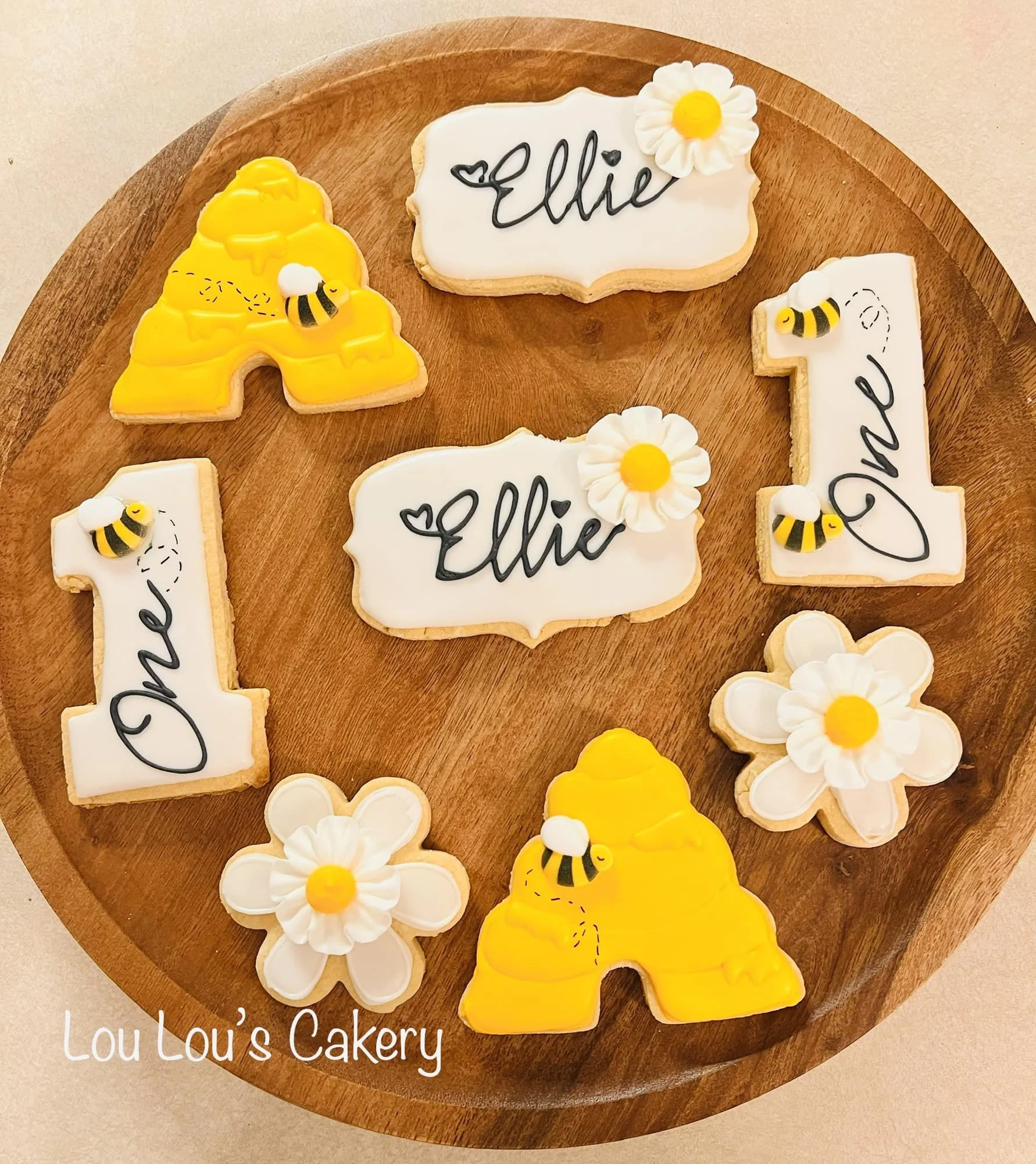 Decorated cookies on a wooden tray with the words "Ellie" and the number "1," featuring bee and flower designs.