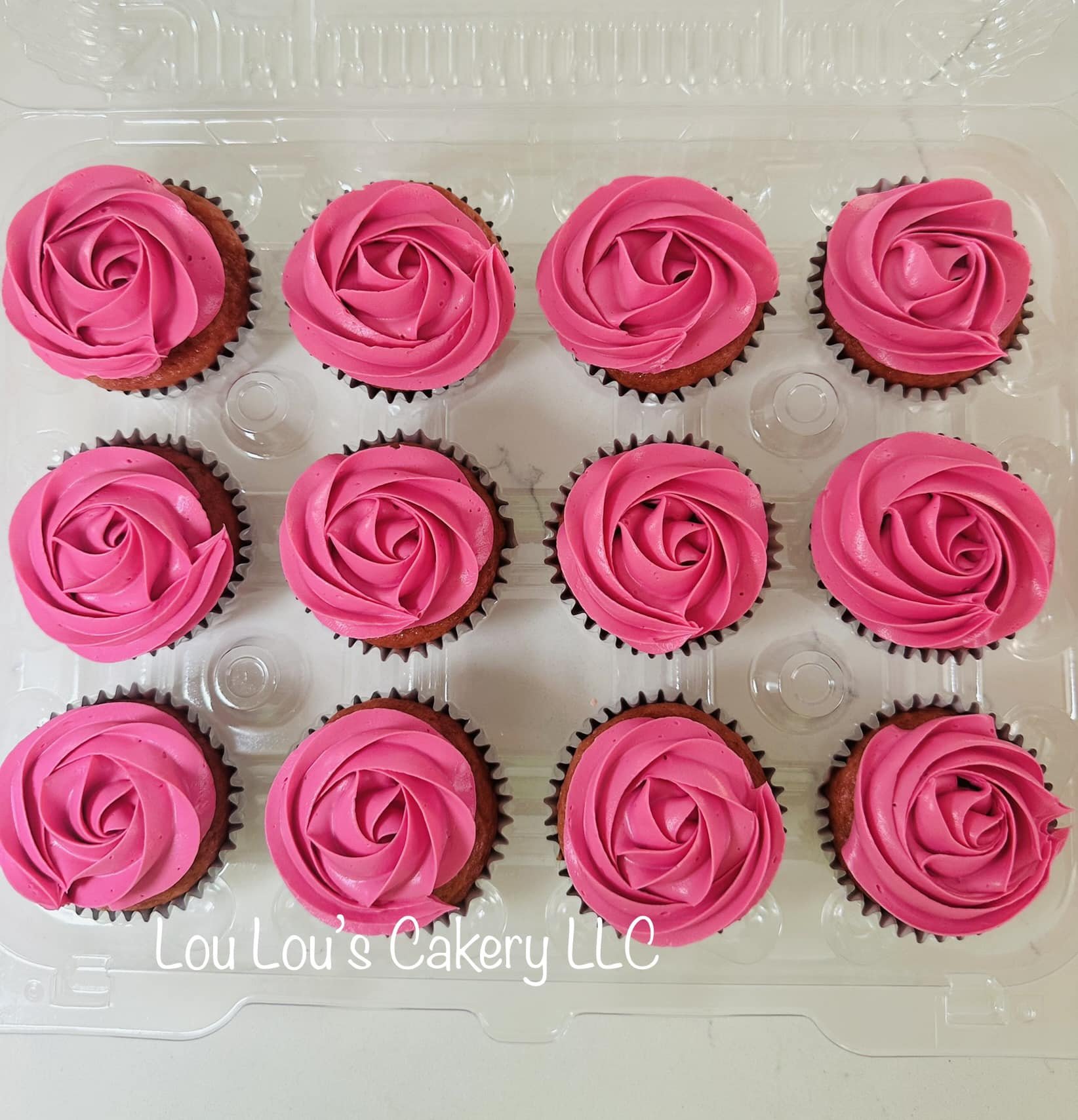 A transparent plastic tray with 15 cupcakes, each decorated with pink rose-shaped frosting swirls.