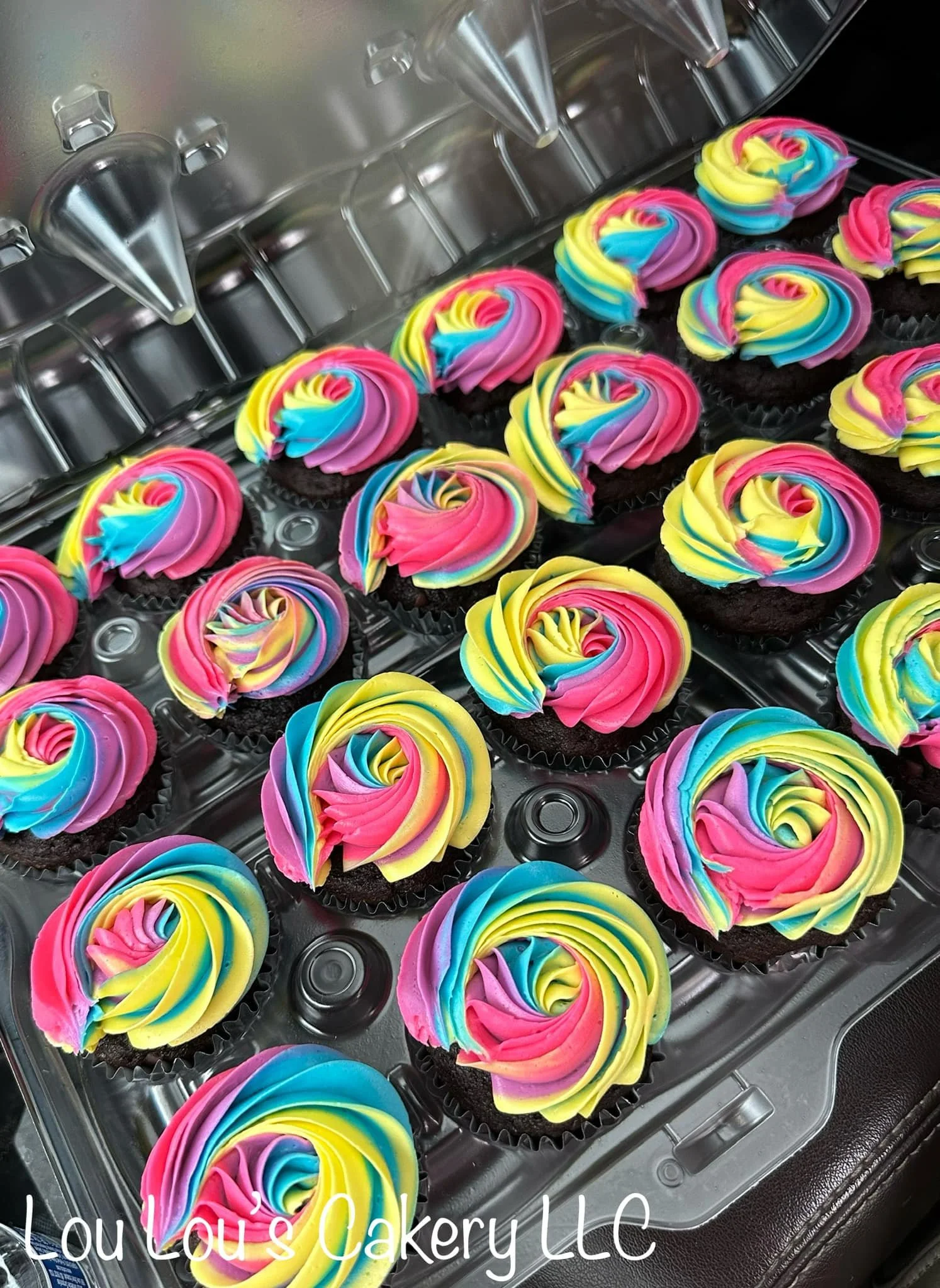 Colorful rainbow swirl cupcakes with vibrant pink, yellow, blue, green, and purple frosting in a bakery display case.