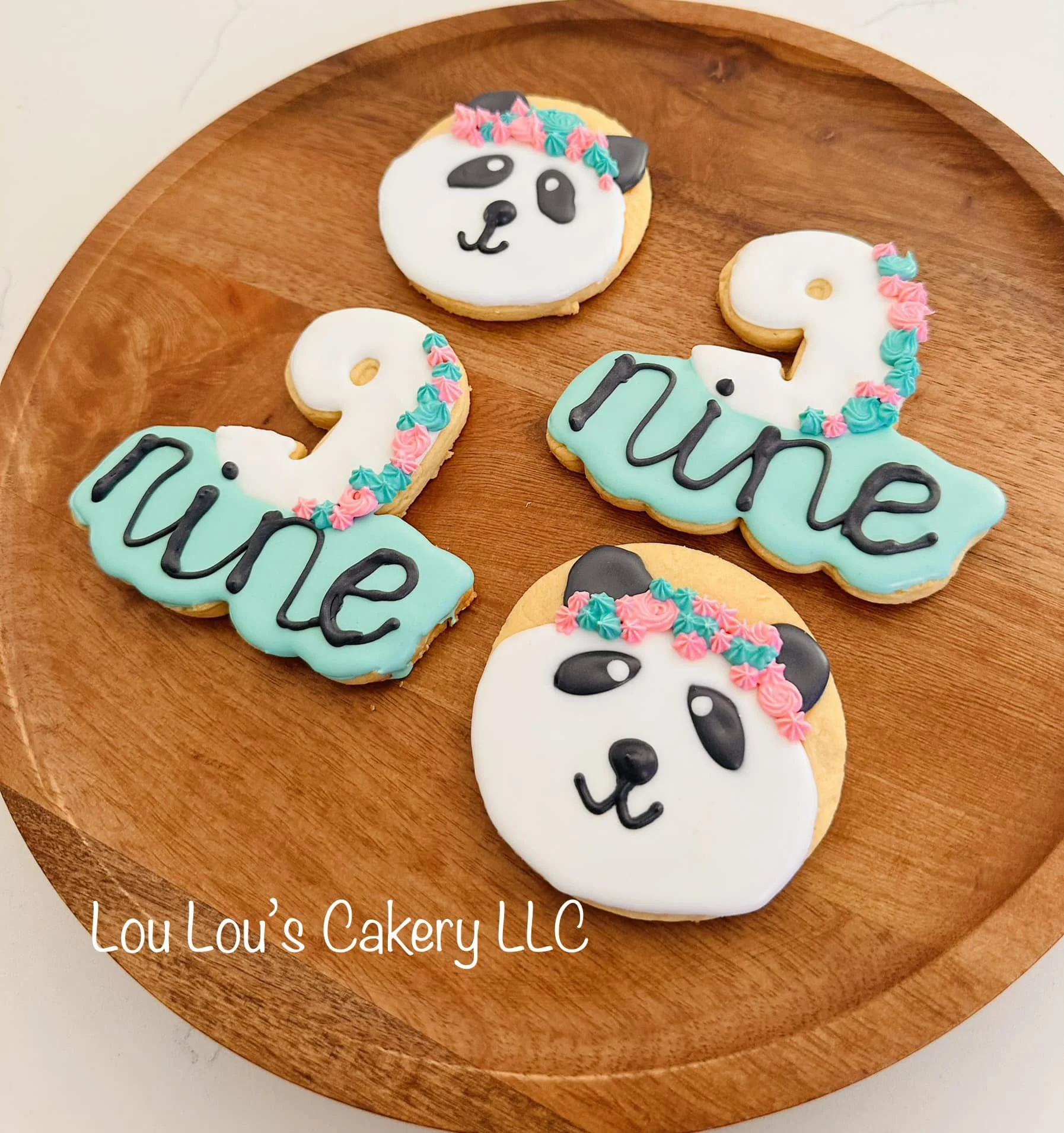 Decorative cookies on a wooden tray with panda faces and the words "love" and "true" written on them in black icing, topped with colorful pink and turquoise frosting accents.