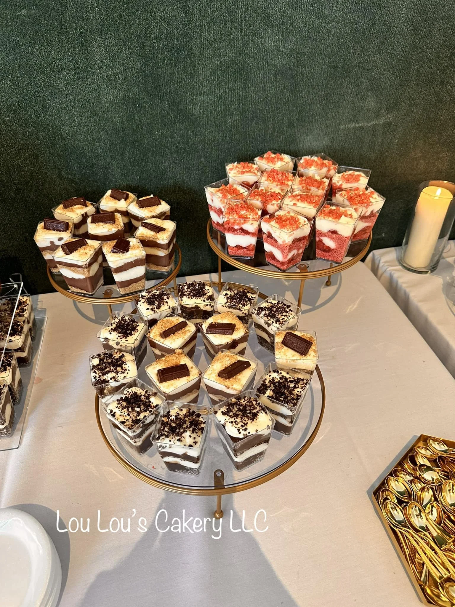 Assorted layered parfaits with chocolate, vanilla, and strawberry flavors, topped with crumbles and chocolate pieces, displayed on tiered trays at a catering event.