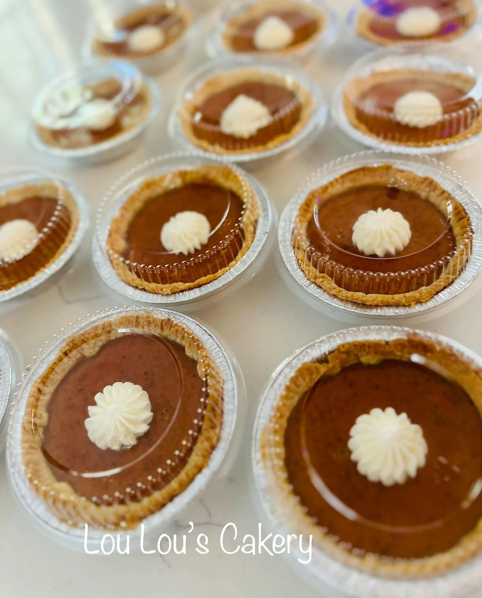 Multiple individual chocolate tartlets with a dollop of white cream on top, placed in clear plastic containers, with the text 'Lou Lou's Cakery' at the bottom.
