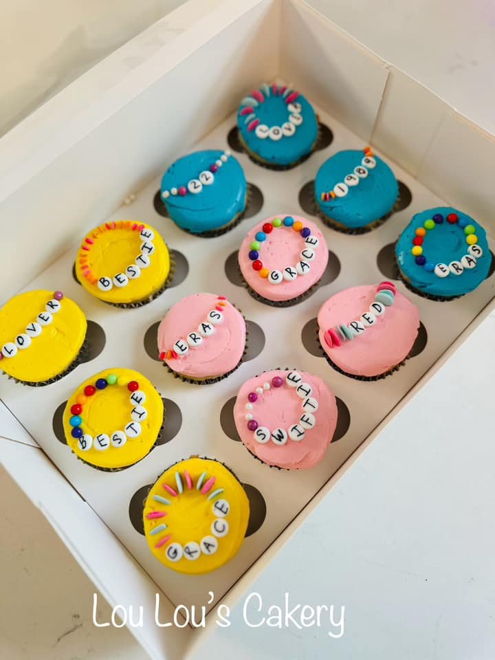 Box of decorated cupcakes with colorful frosting and sprinkles, each cupcake has a word spelled with letter beads, forming messages like 'LOVE DESTINY', 'BESTIE', 'GRACE', and 'MIRED'.