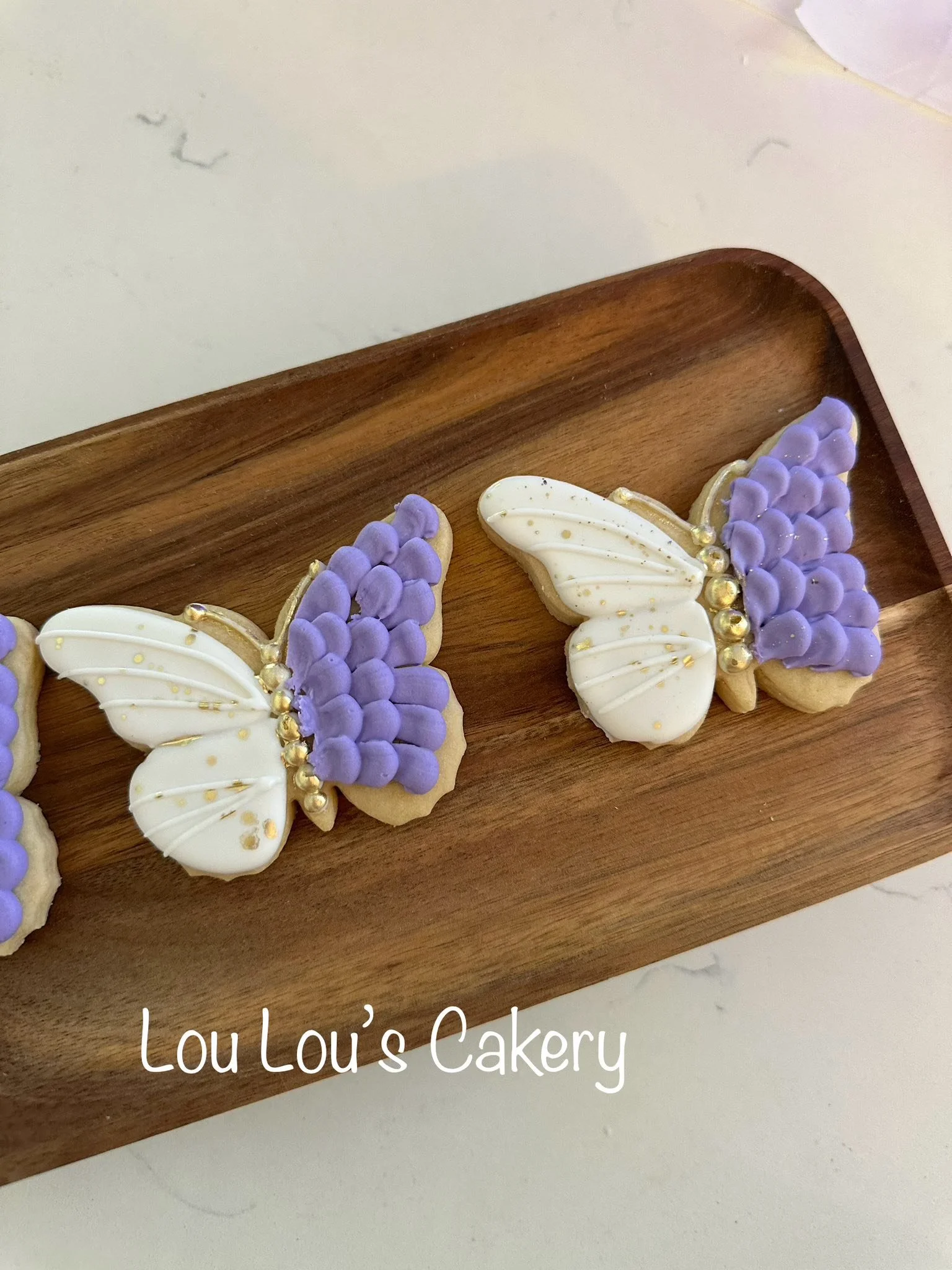 Decorated butterfly-shaped cookies with purple and white icing on a wooden tray.