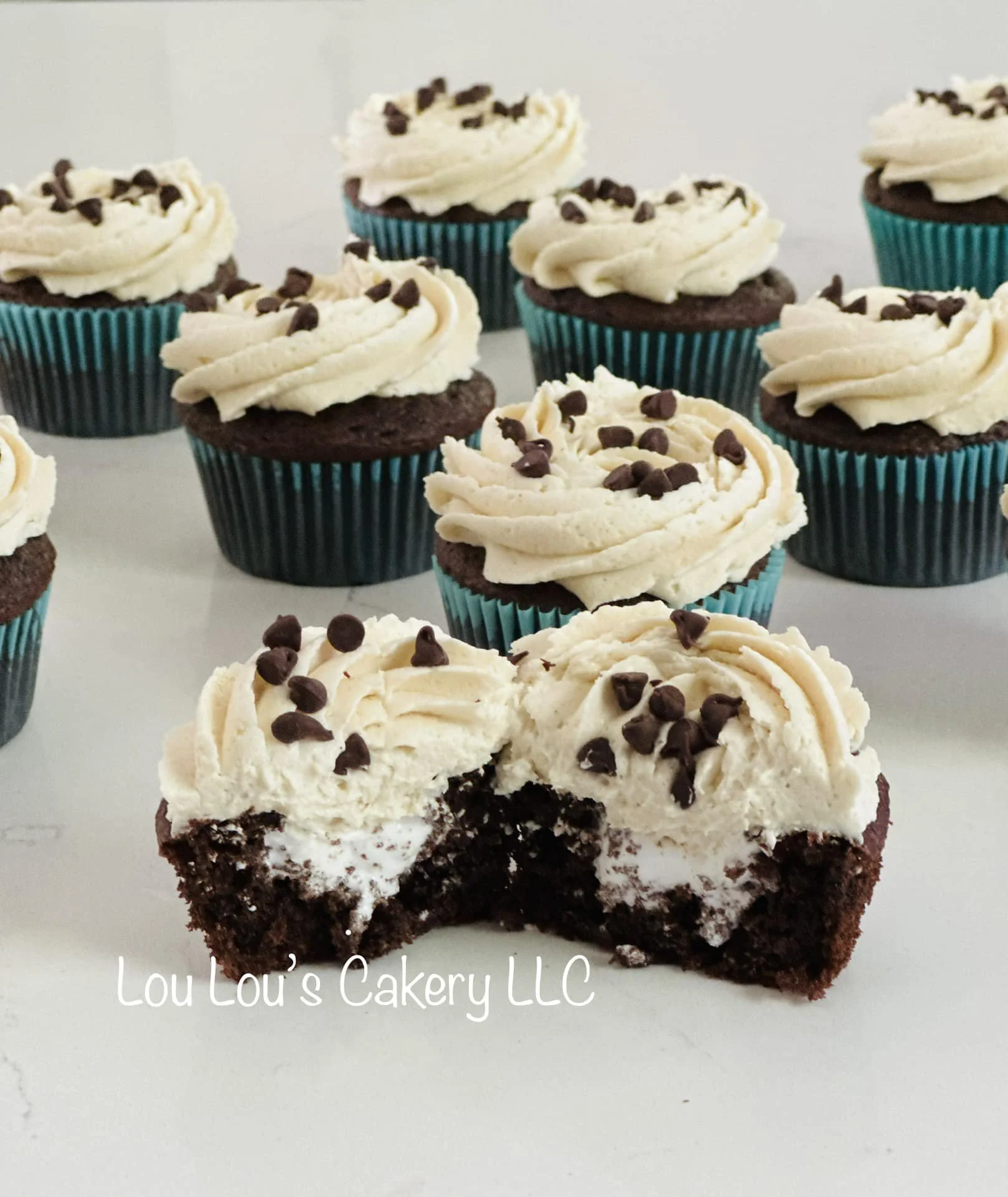 Chocolate cupcakes with vanilla frosting and chocolate sprinkles, with one cupcake cut in half to show chocolate and cream filling, text overlay reads 'Lou Lou's Cakery LLC'.
