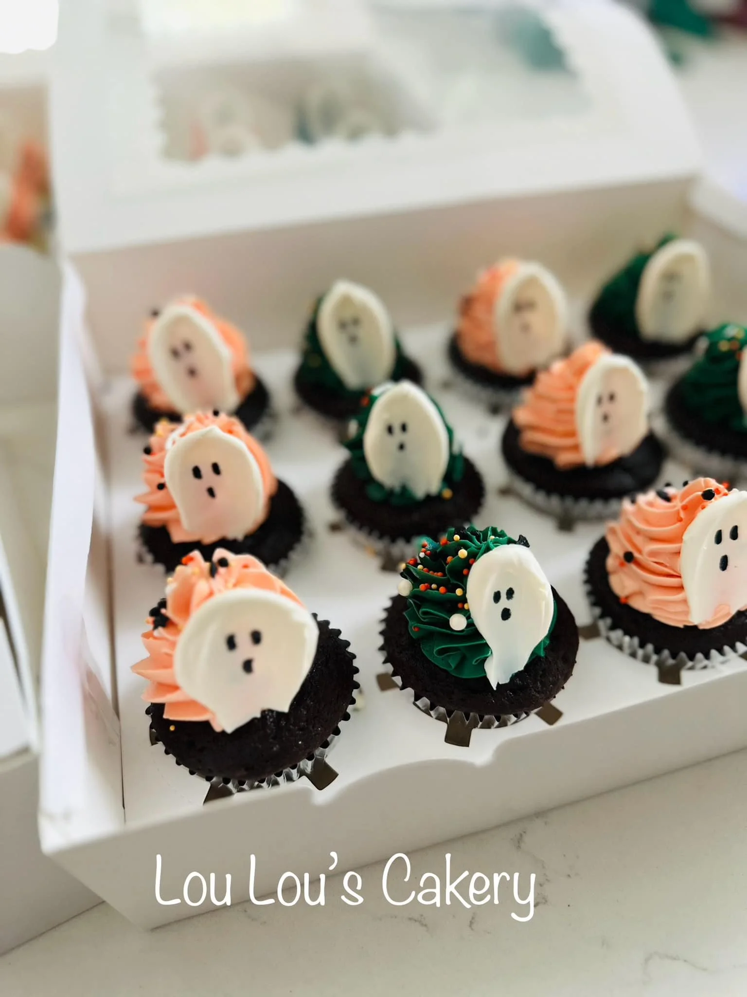 Box of Halloween-themed cupcakes with ghost and pumpkin decorations from Lou Lou's Cakery.