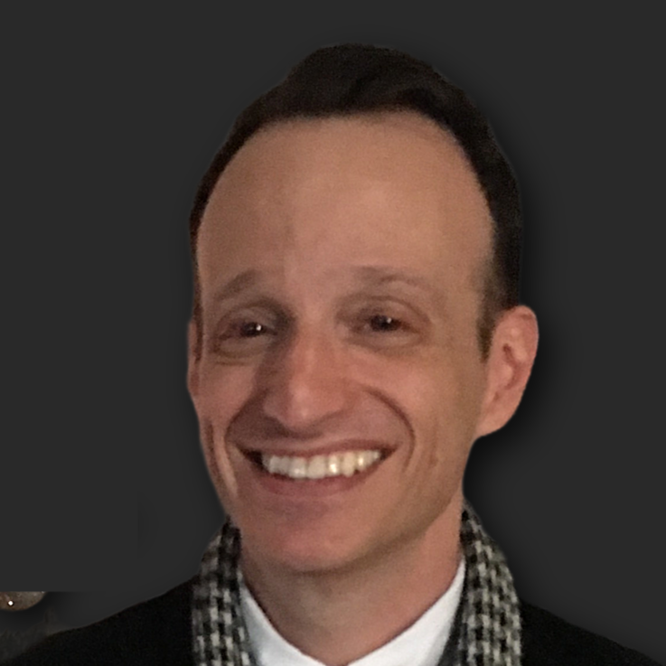 A smiling man with short dark hair, wearing a checkered scarf and black jacket, against a dark background.