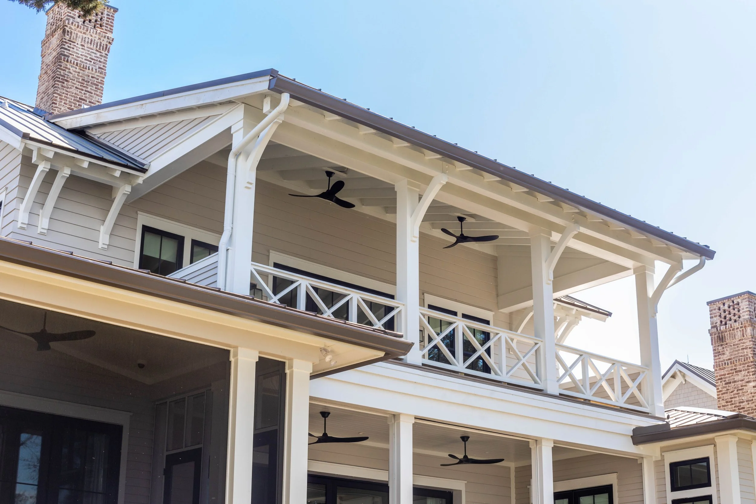 Crane Island Home. Exterior view of a house showing a two-story porch with white railings, ceiling fans, and a roof with exposed rafters and a chimney.