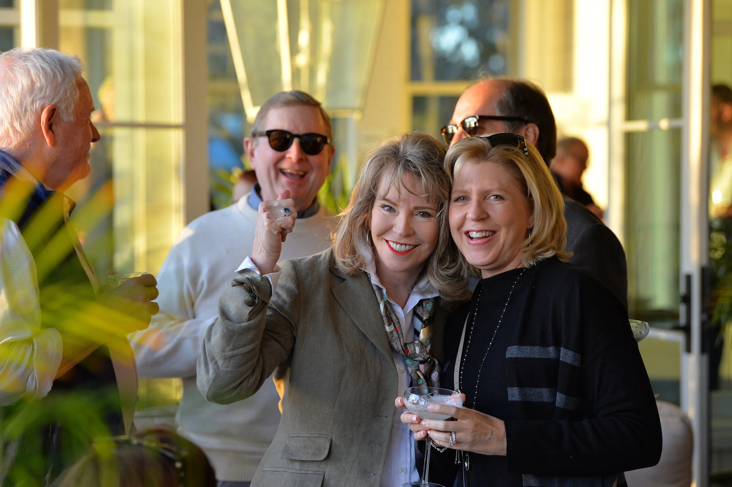 Crane Island Events. Group of people smiling and enjoying a social gathering indoors, with sunlight streaming through windows.