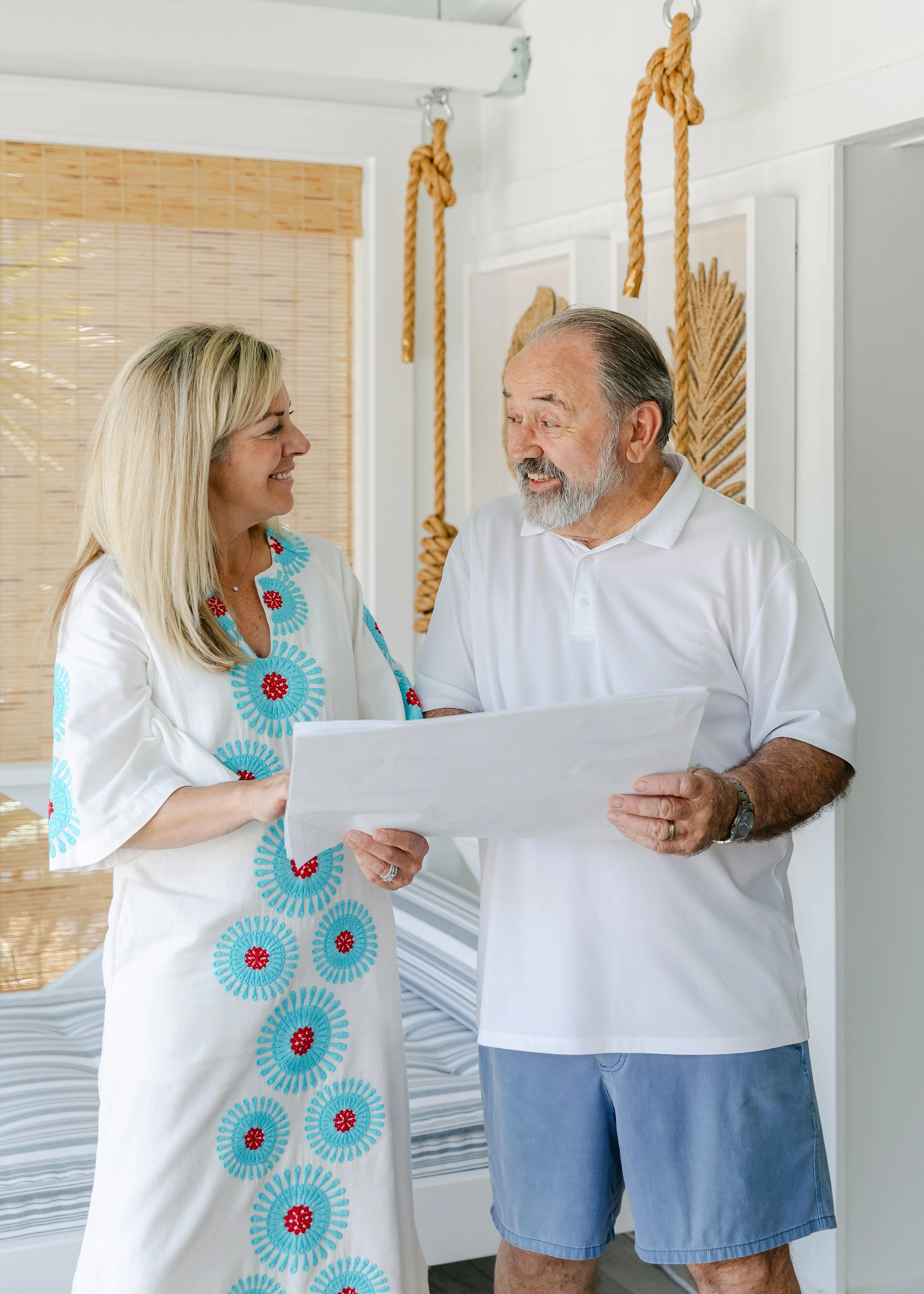 Cabana Lane - Builders at Crane Island. A middle-aged man and a woman in white shirts talking and smiling inside a bright room with wall art and hanging ropes.