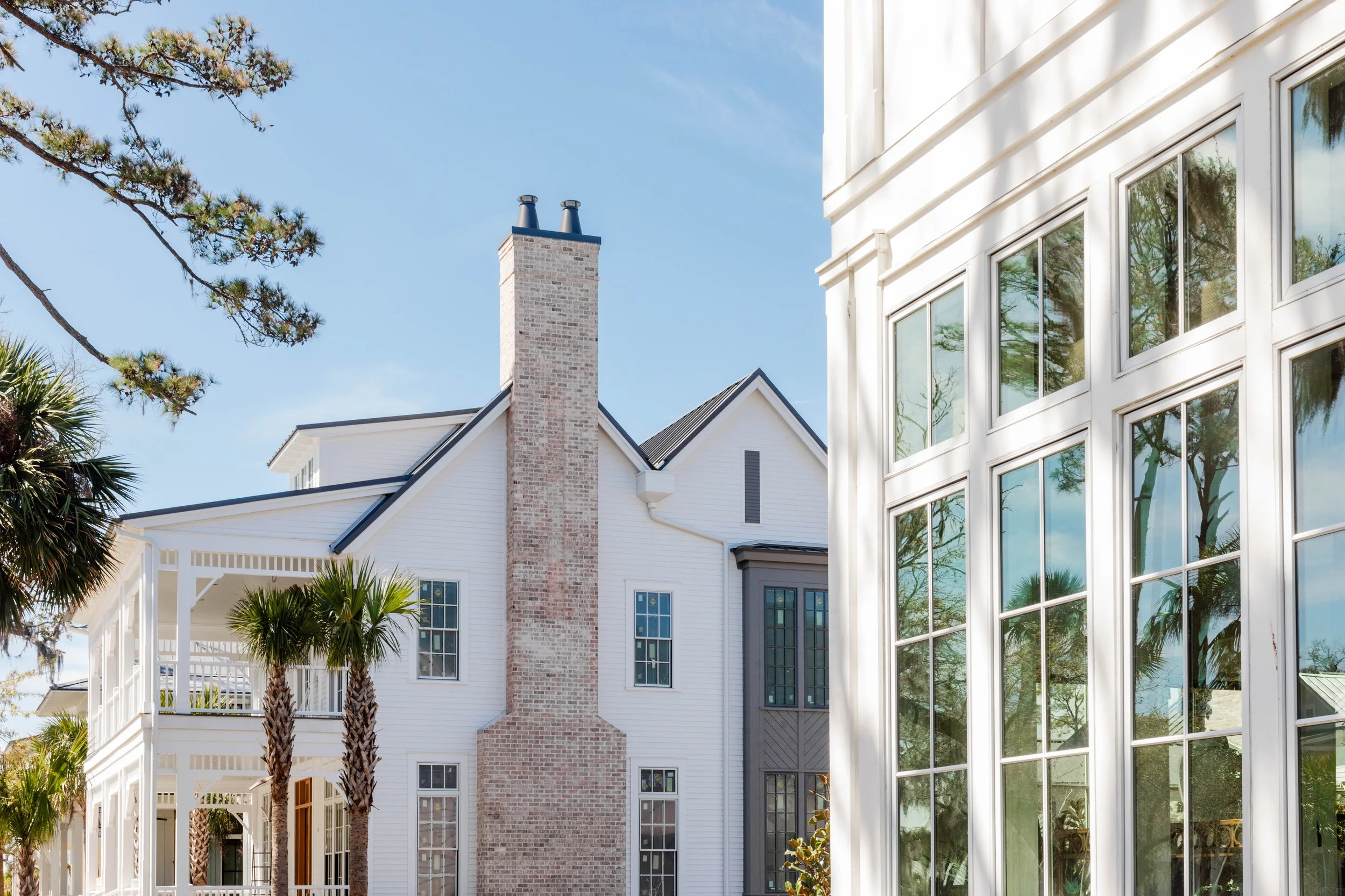 Park District at Crane Island. Exterior of a white house with a brick chimney, large windows, and palm trees, under a blue sky.