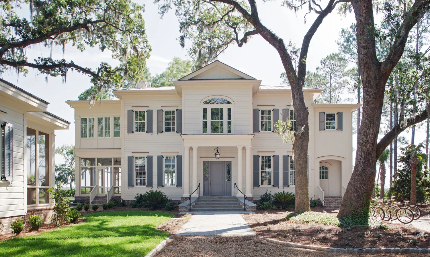 A large two-story white house with gray shutters, a front porch, steps, a pathway, trees, and a lawn.
