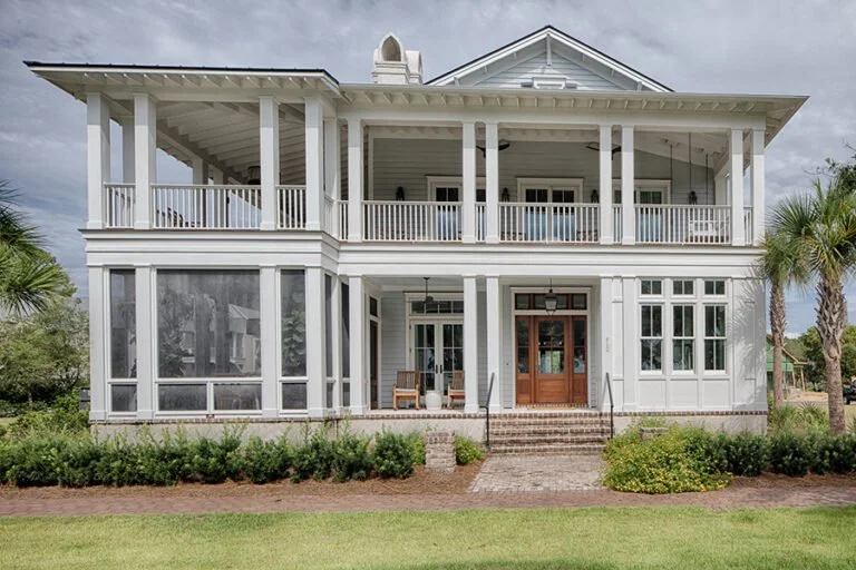 Pearce Scott Architects - Crane Island. Large two-story house with white exterior and expansive wraparound porch, set in a green yard with palm trees.