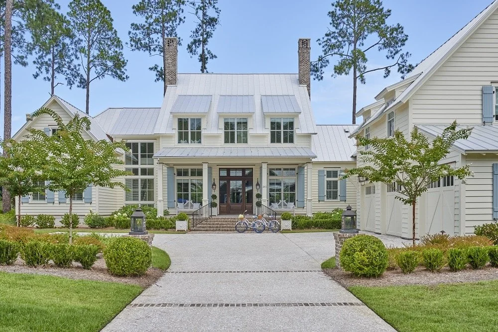Court Atkins Architects - Crane Island. Large white house with a metal roof, multiple windows, and front porch, surrounded by trees and manicured shrubbery.