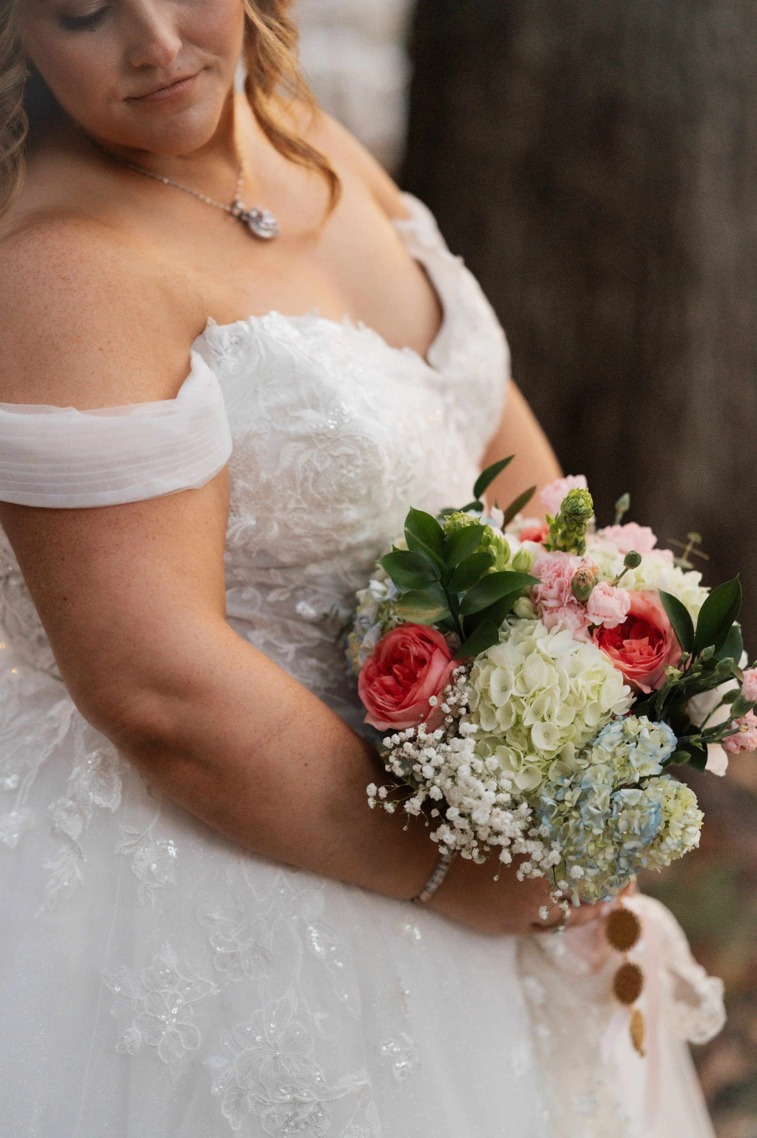 Close-up of a woman in a white wedding dress holding a colorful bouquet of flowers, with only part of her face and dress visible.