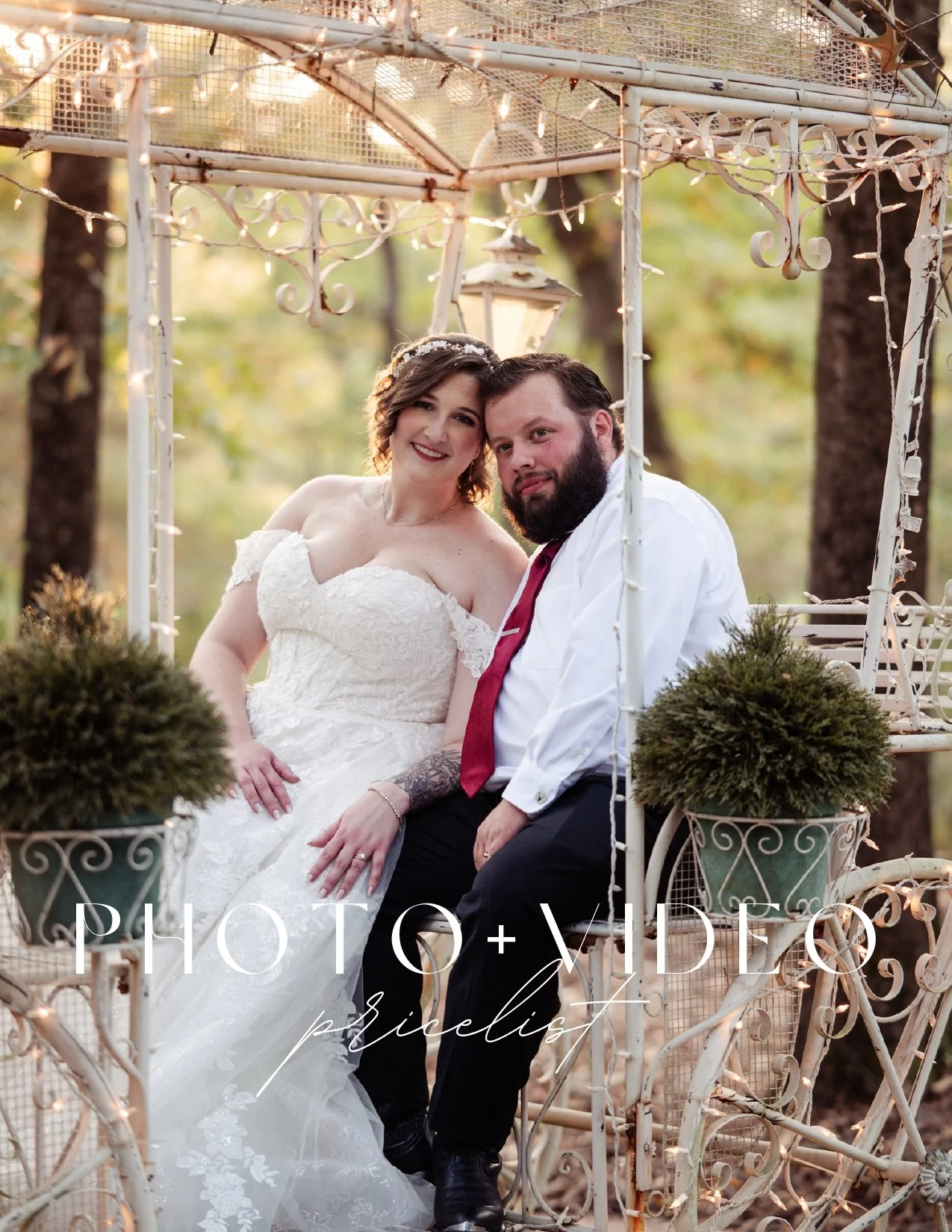 A bride and groom sitting together on a decorative white metal garden swing outdoors during sunset, with trees in the background and fairy lights hanging overhead.