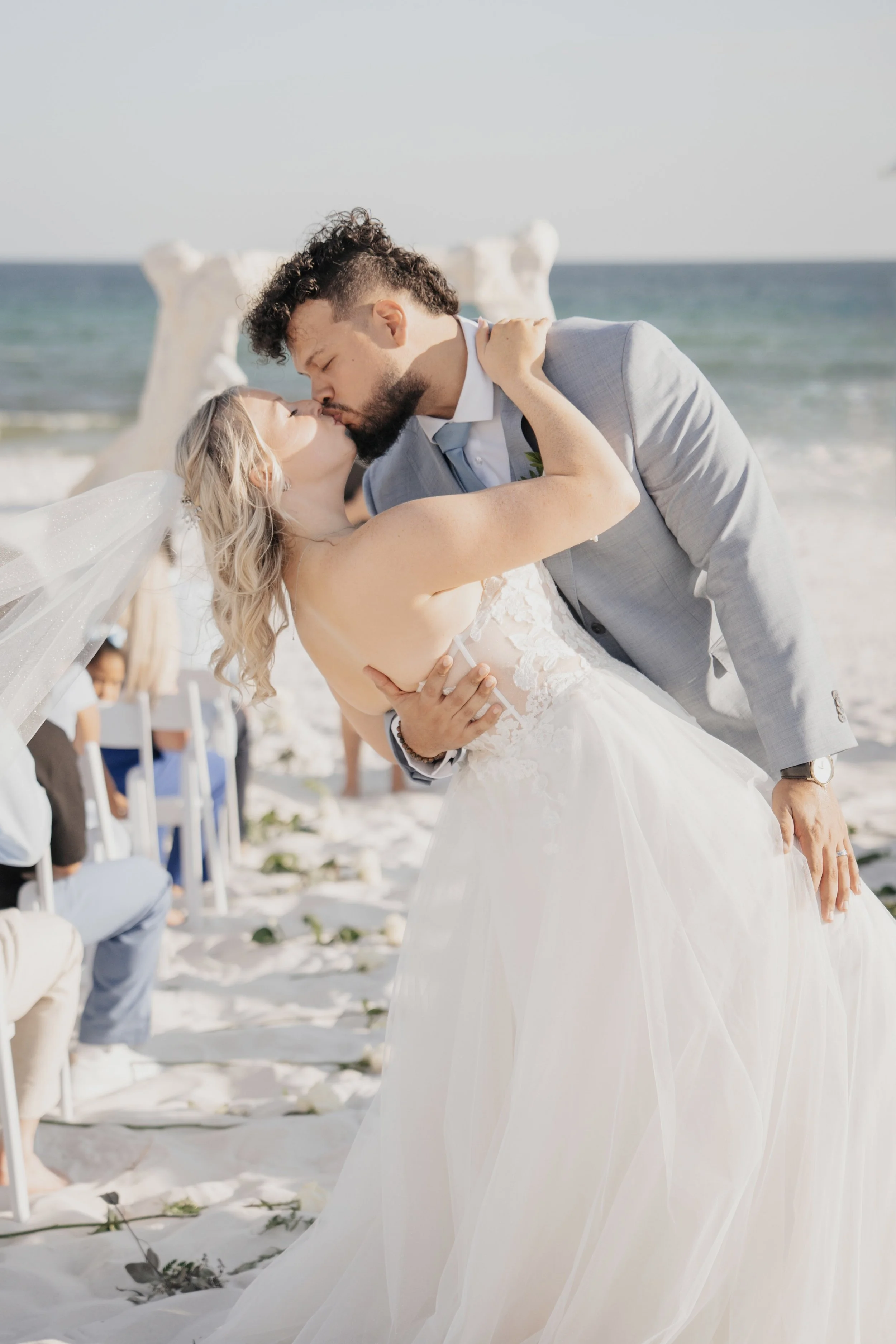A bride and groom sharing a kiss during their beach wedding ceremony.