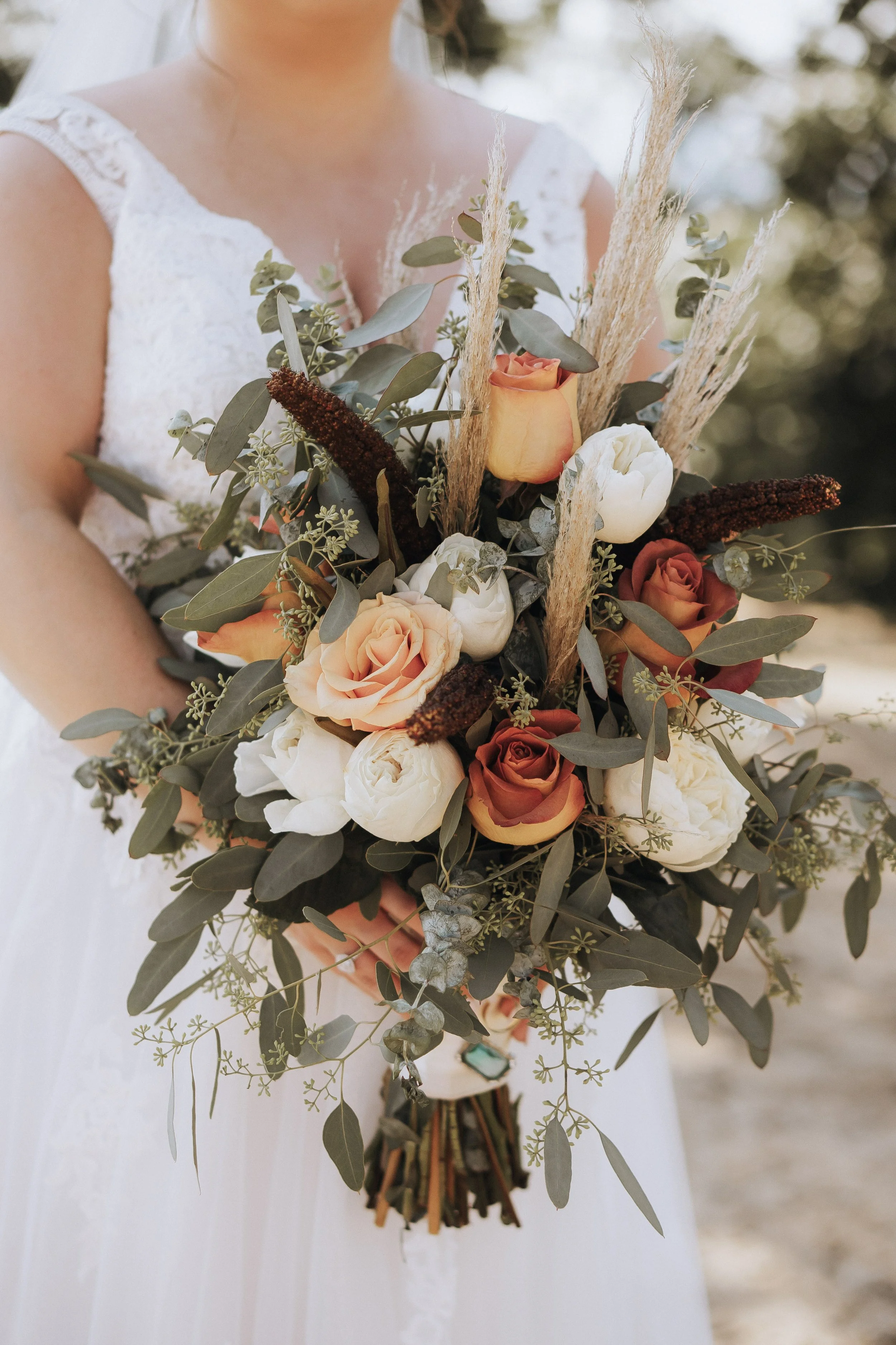 Close-up of a bride holding a bouquet of roses, peonies, eucalyptus, and pampas grass.