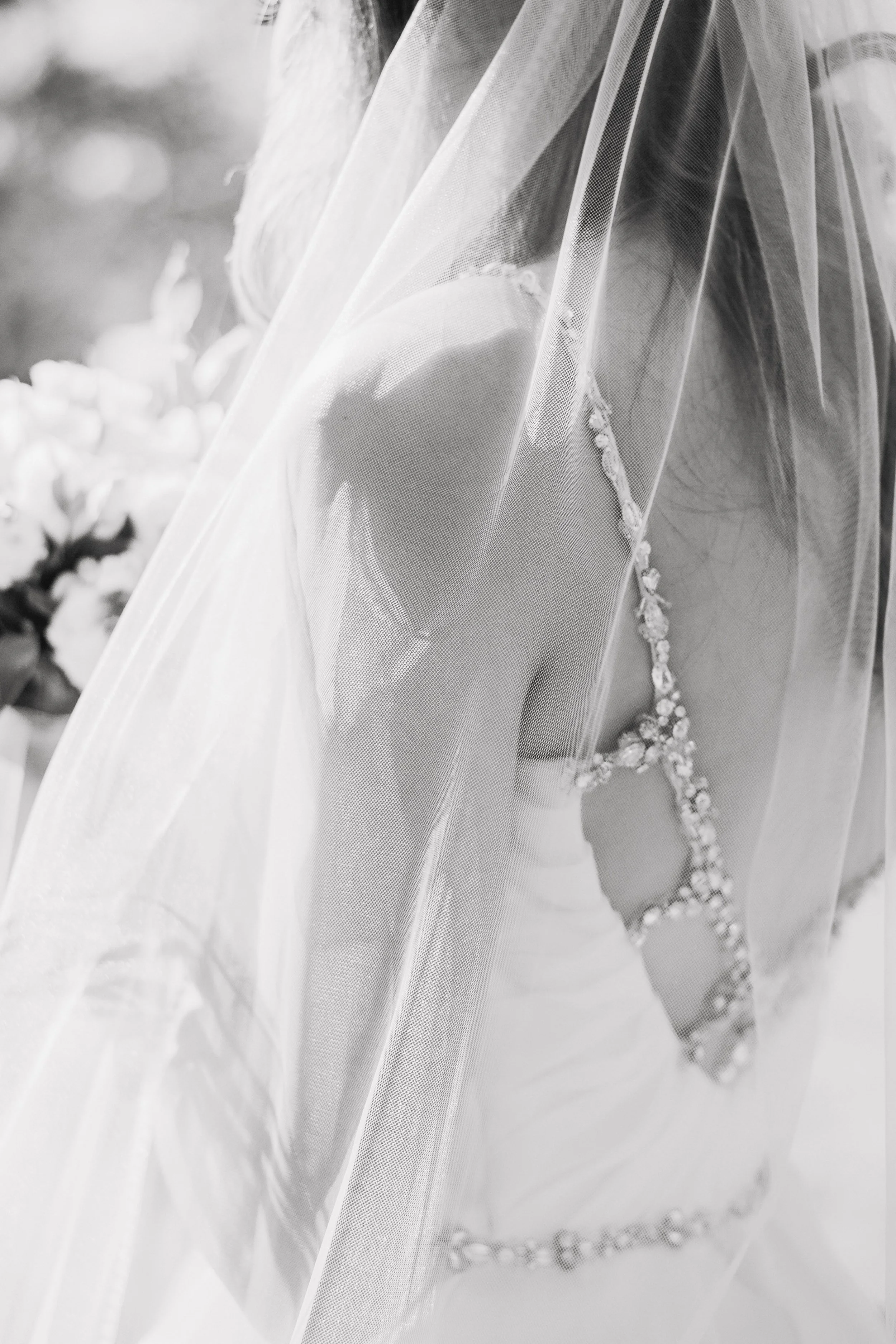 Close-up of a bride in a wedding dress and veil, with decorative details, under soft light.